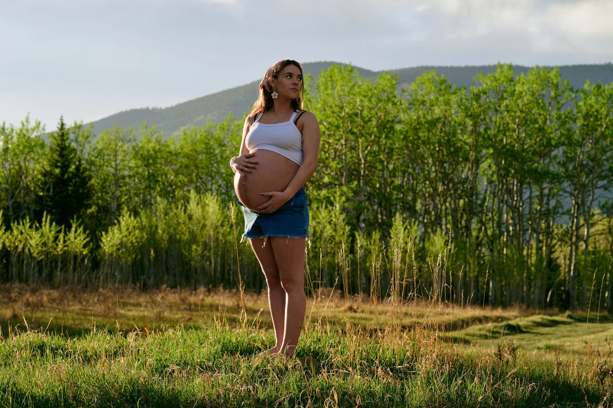 White tank and denim shorts in an aspen-lined meadow, classic summer maternity photos in the mountains.