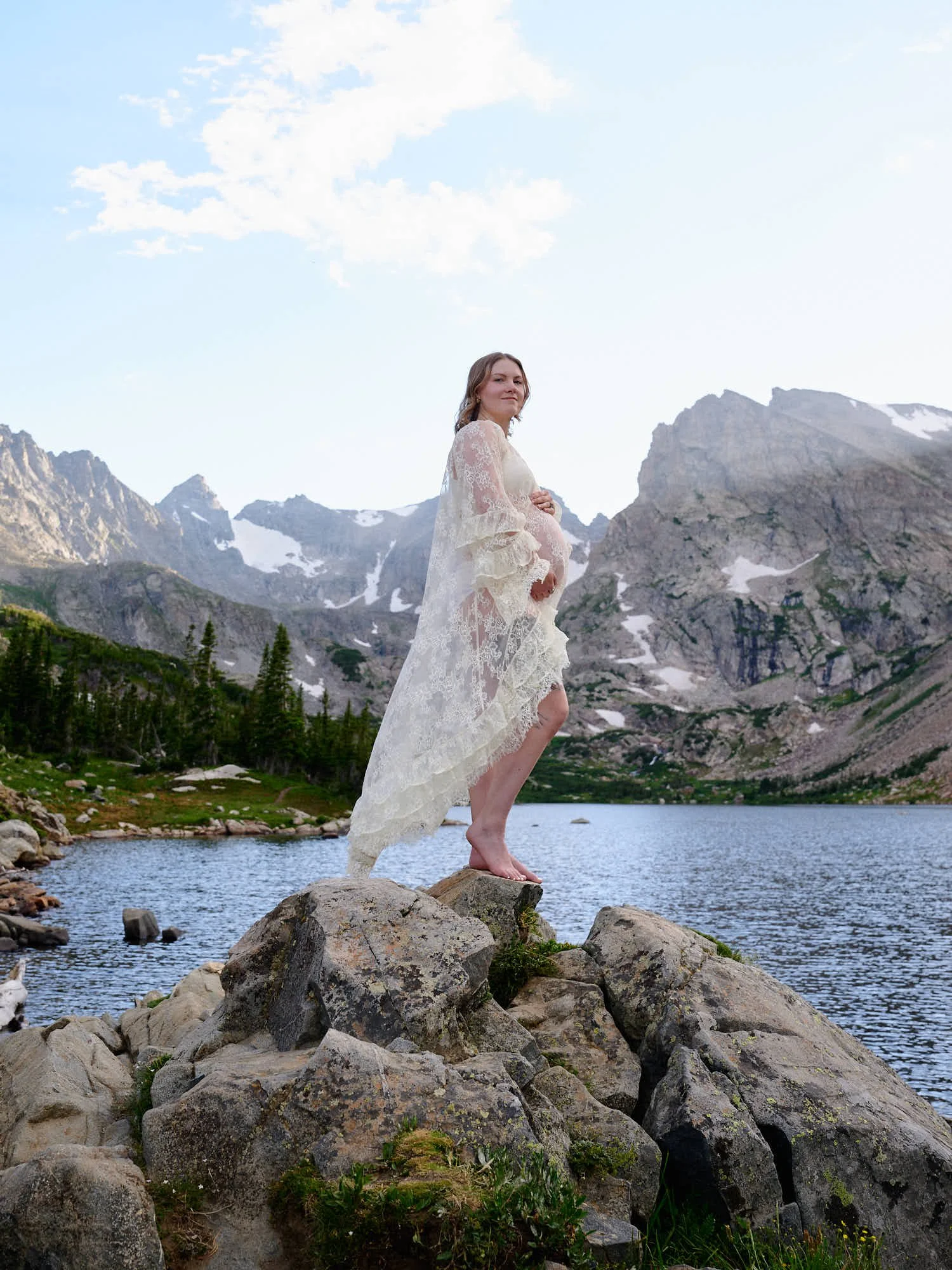White gown on a boulder at the shore of Lake Isabelle, the Indian Peaks rising behind.