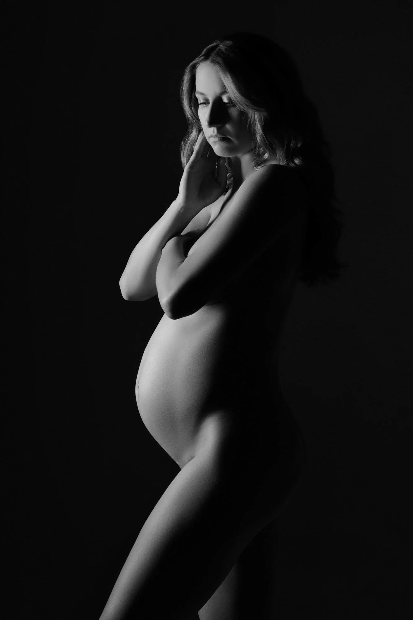 Sculpting light shapes an expecting mother's profile in classic black and white fine art style.