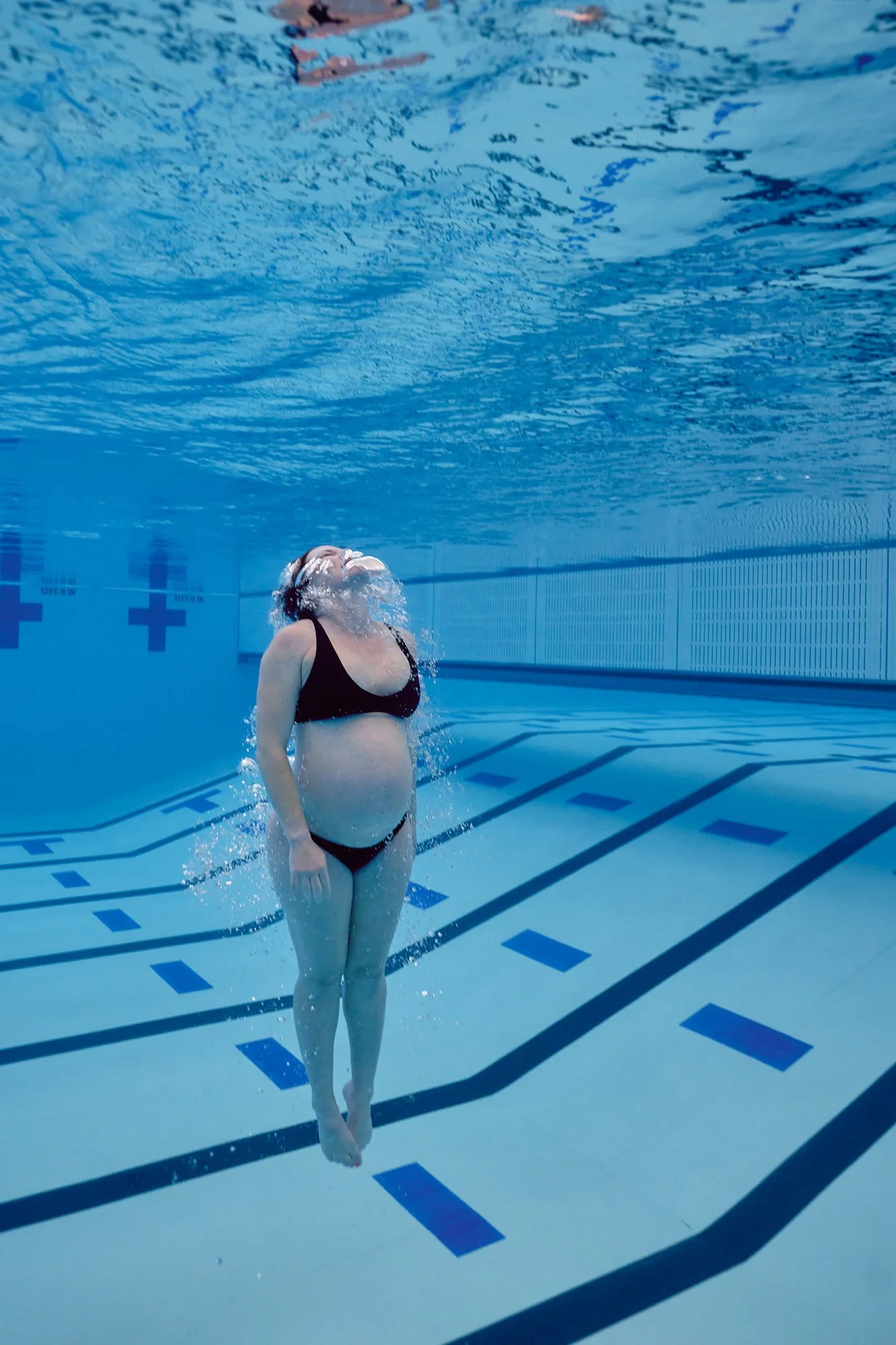 Underwater portrait, an expecting diver upright in blue water looking toward the surface.