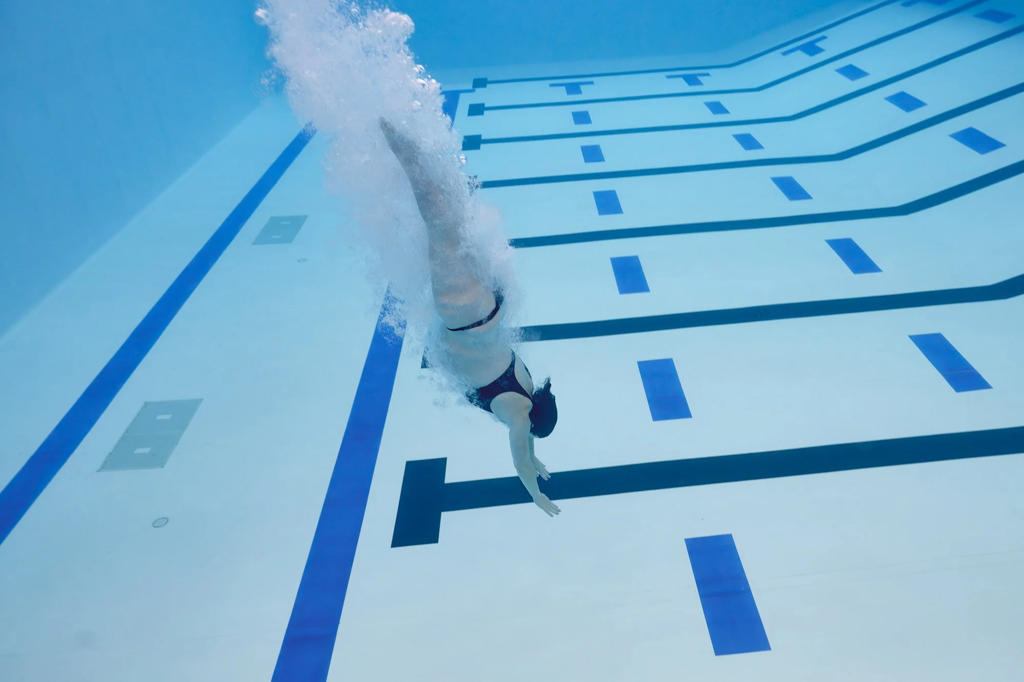 Descending toward the pool floor underwater, body arrow straight along the lane lines.
