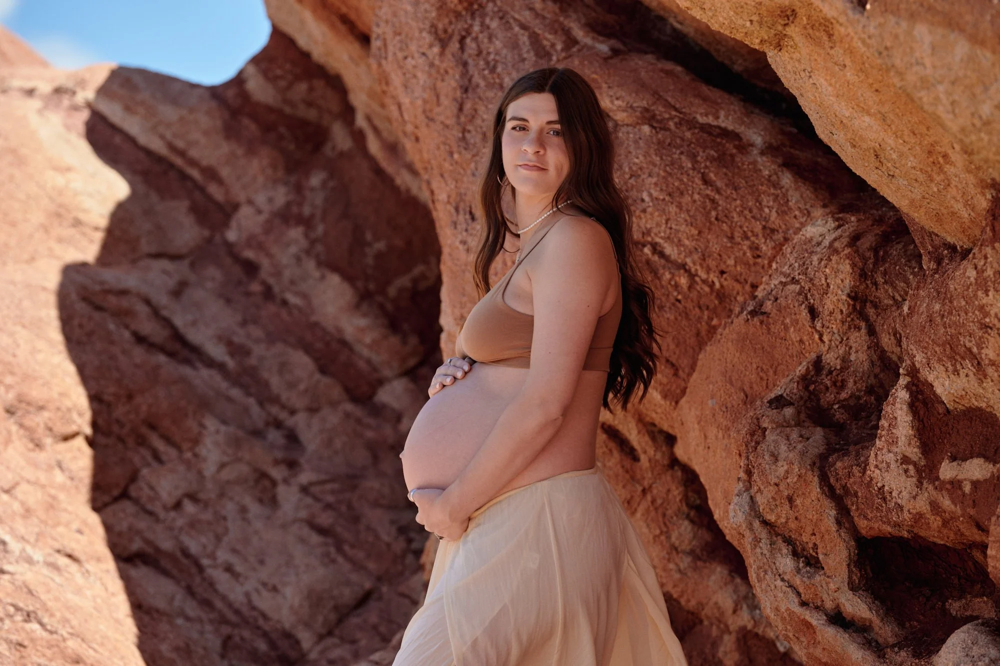 Two-piece in the shade of a red sandstone wall at Garden of the Gods, hand on the bump.