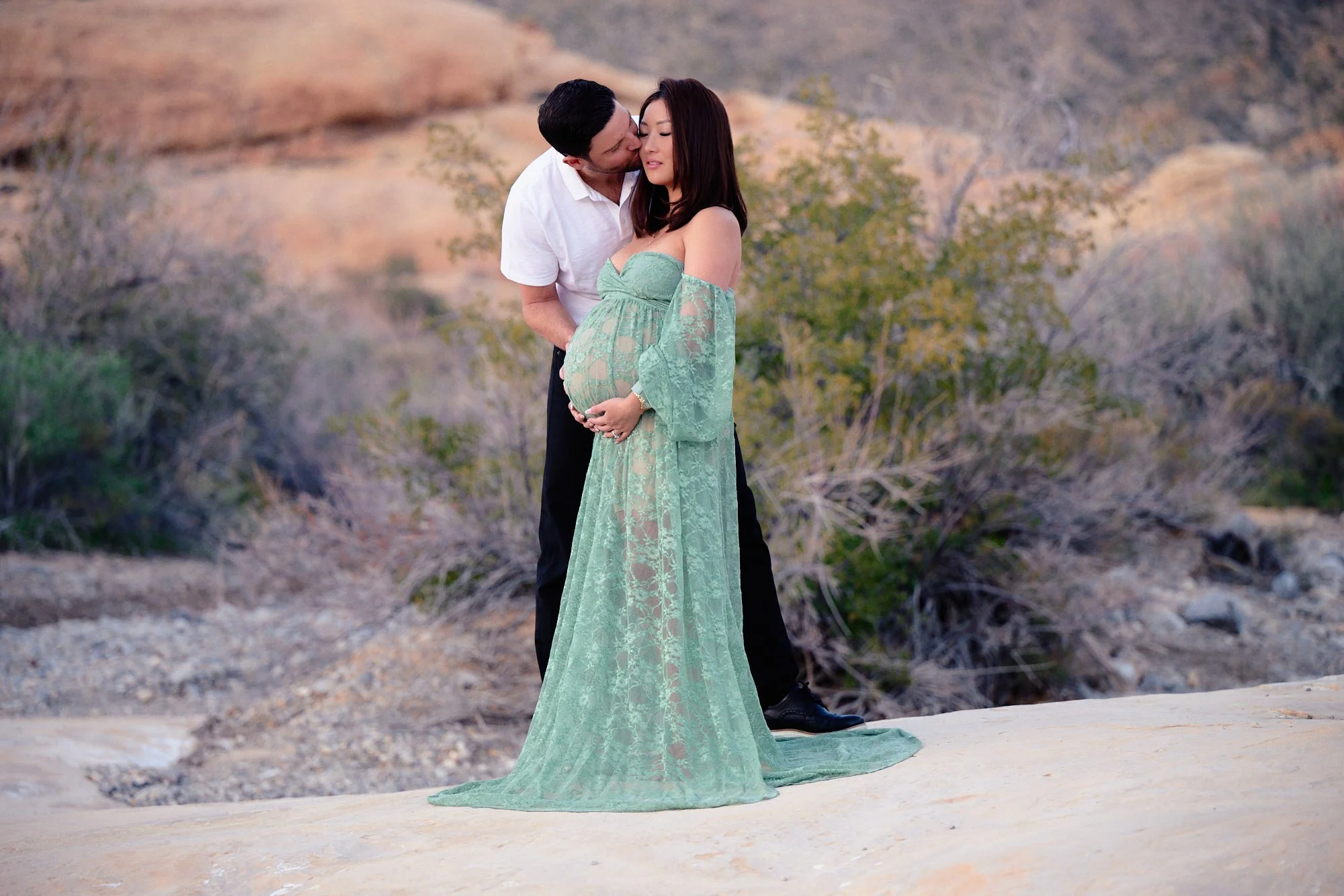 A kiss in Red Rock Canyon, sage lace gown against pale sandstone and desert scrub.