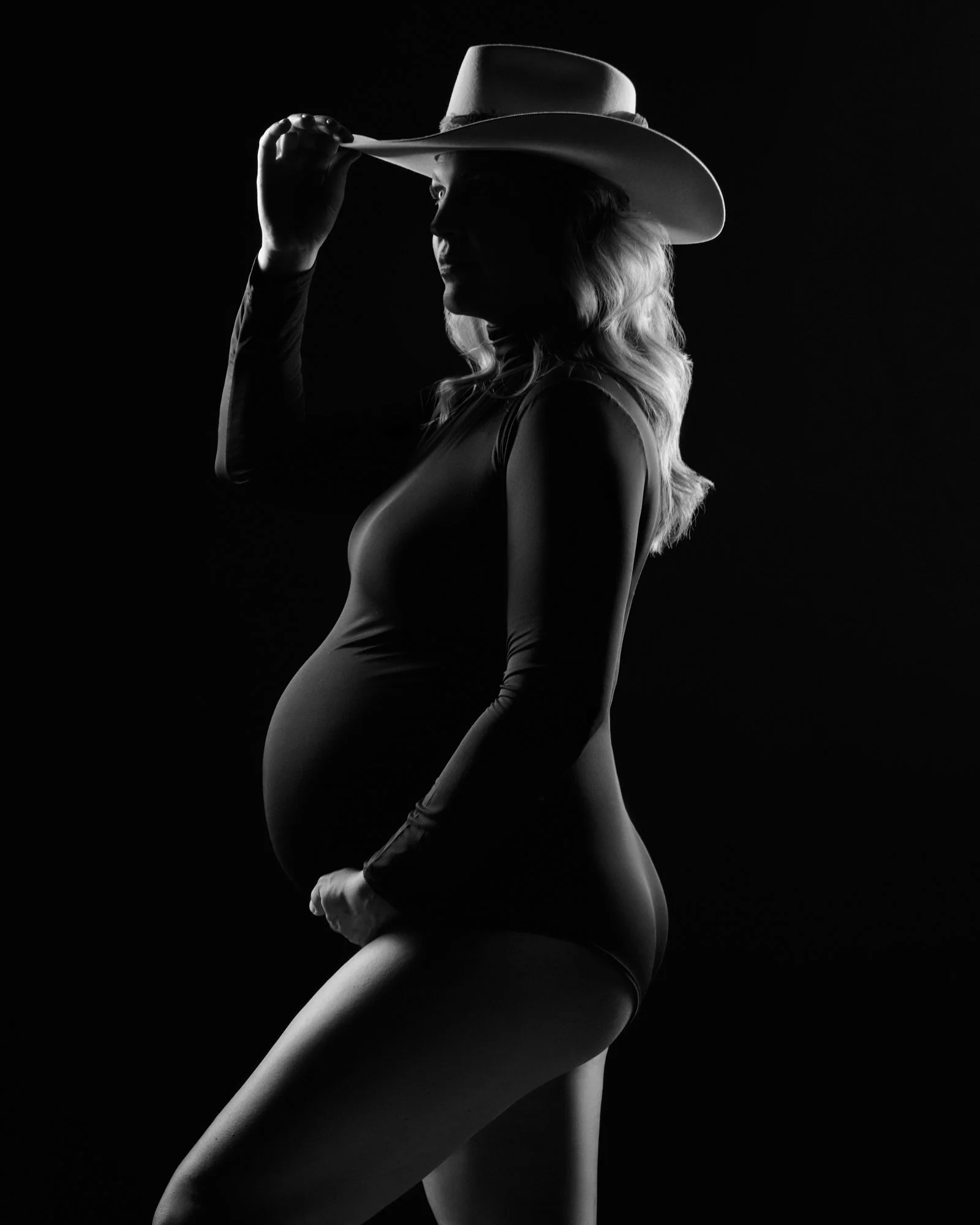White cowboy hat tipped in silhouette, rim light carving the profile from black.