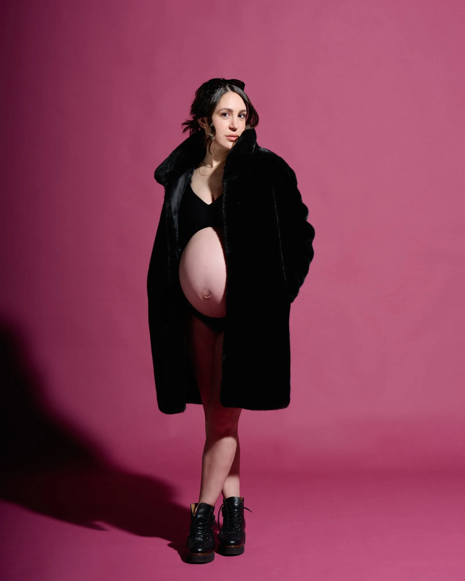 Boots crossed in a black fur coat under hard magenta light, editorial attitude.