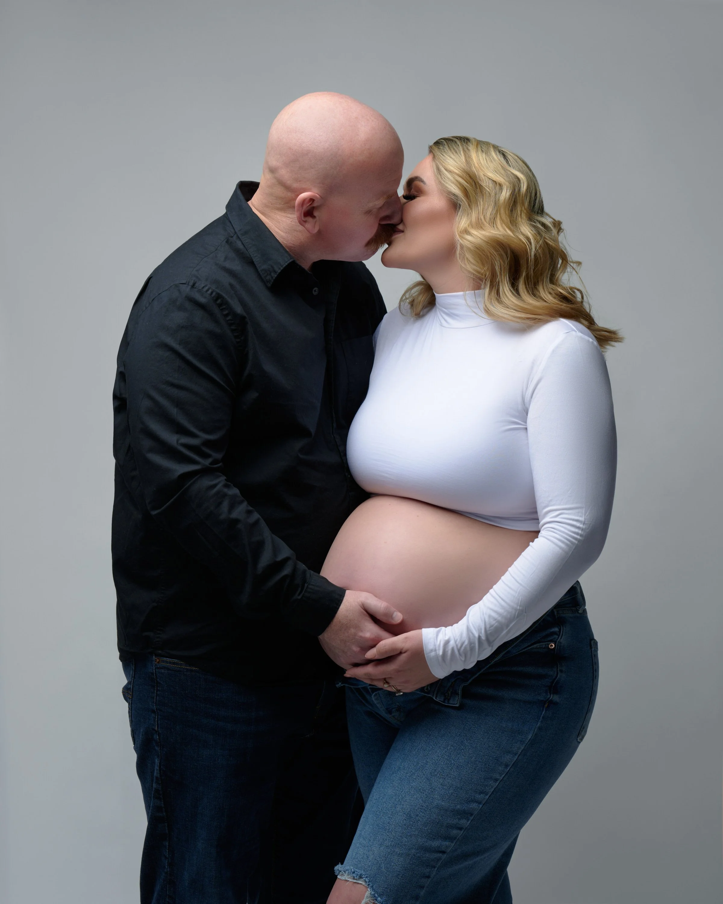 A kiss in a white crop top and ripped jeans, his hand under her bump.