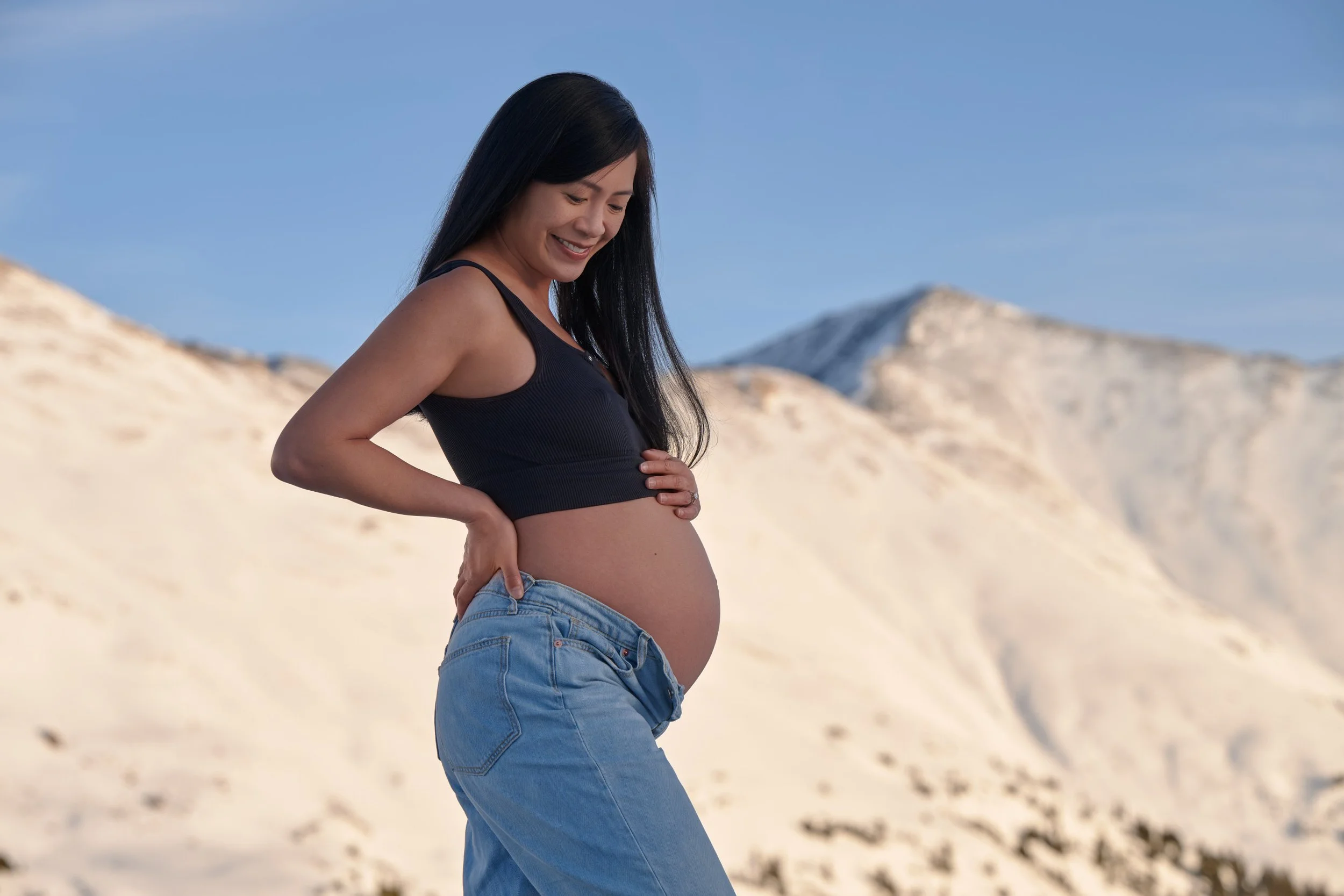 Winter maternity photos on Loveland Pass, bare bump in a black tank against a wall of snow.
