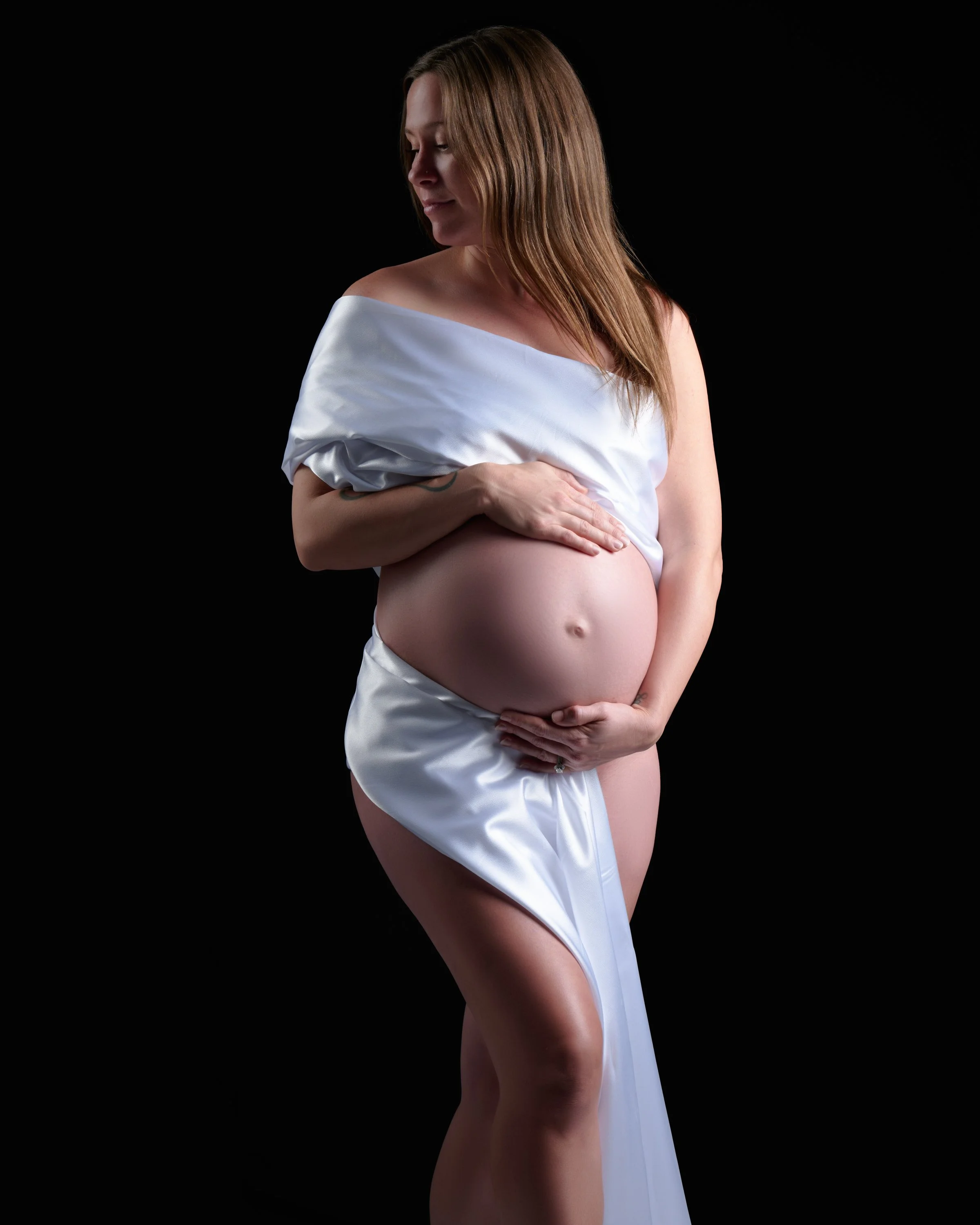 Elegant studio maternity photo with soft white pearl fabric styled in a boudoir-inspired pose in Colorado