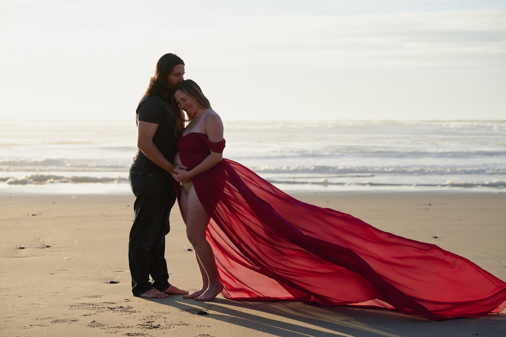 Red gown with a sweeping train on a misty beach, couple embracing at the tide line.