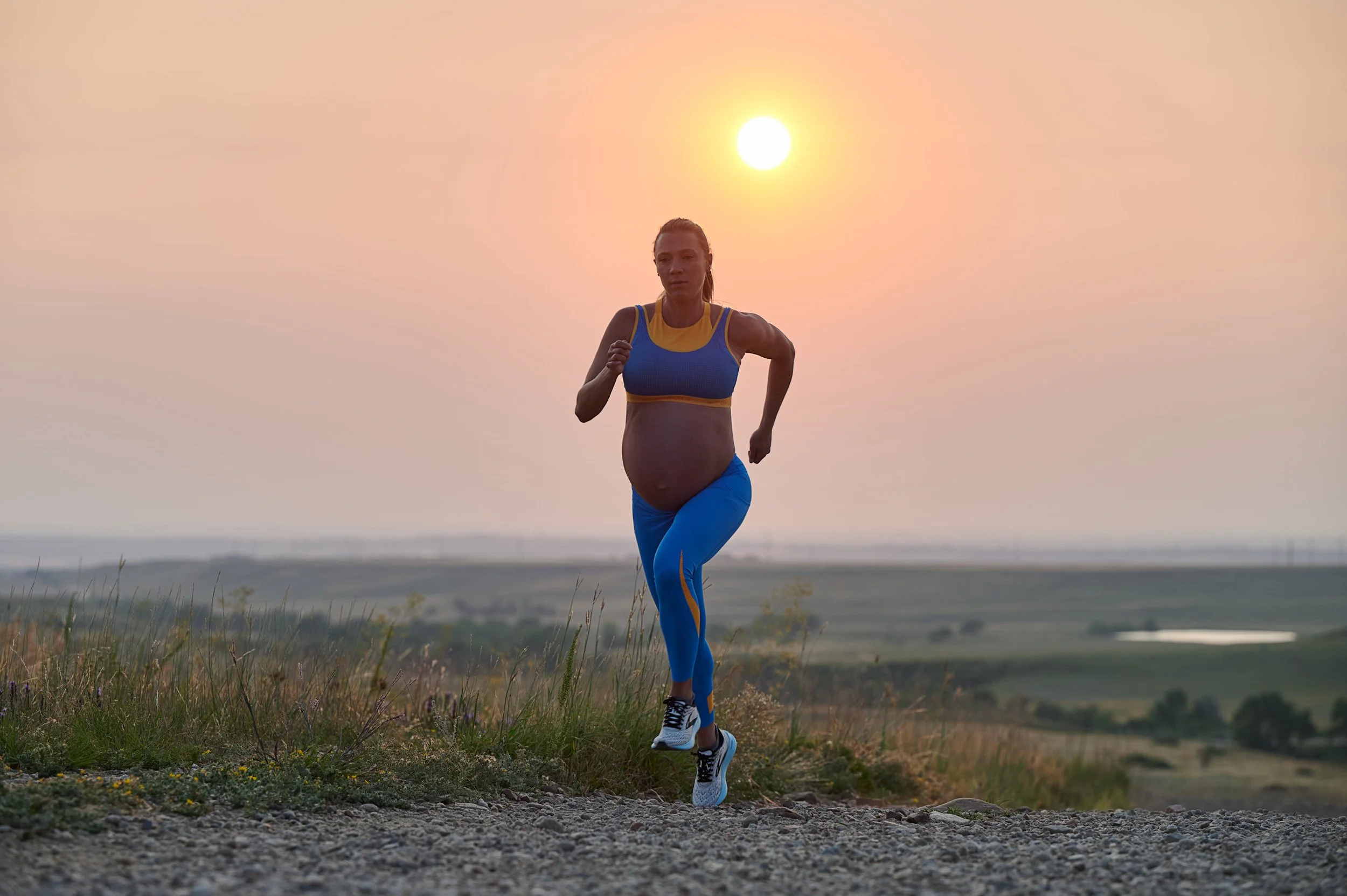 Running toward the sunrise on a gravel path, the plains opening out behind her.