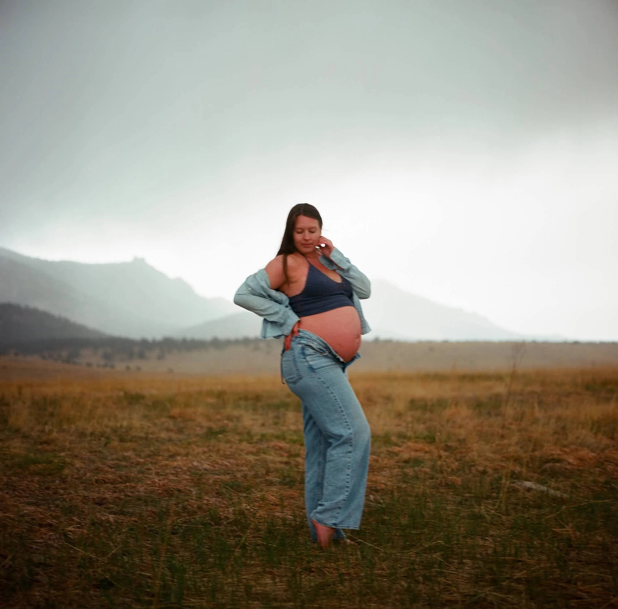 Jeans and a lifted knit top in a dry spring field, fog sitting low on the peaks.
