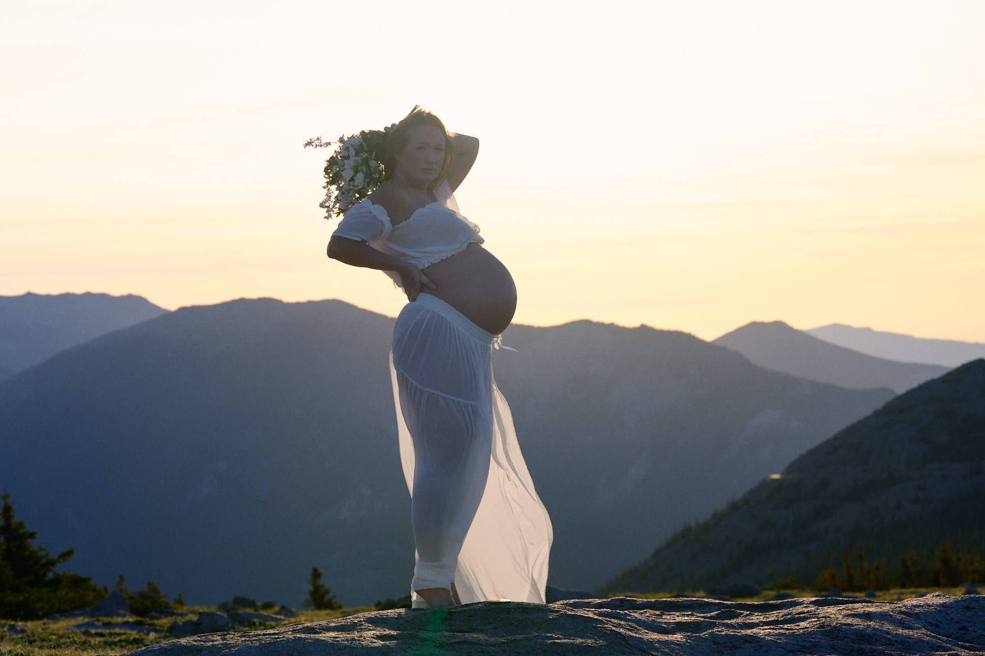 Golden backlight rims a white crop top and sheer skirt on a mountaintop granite slab.