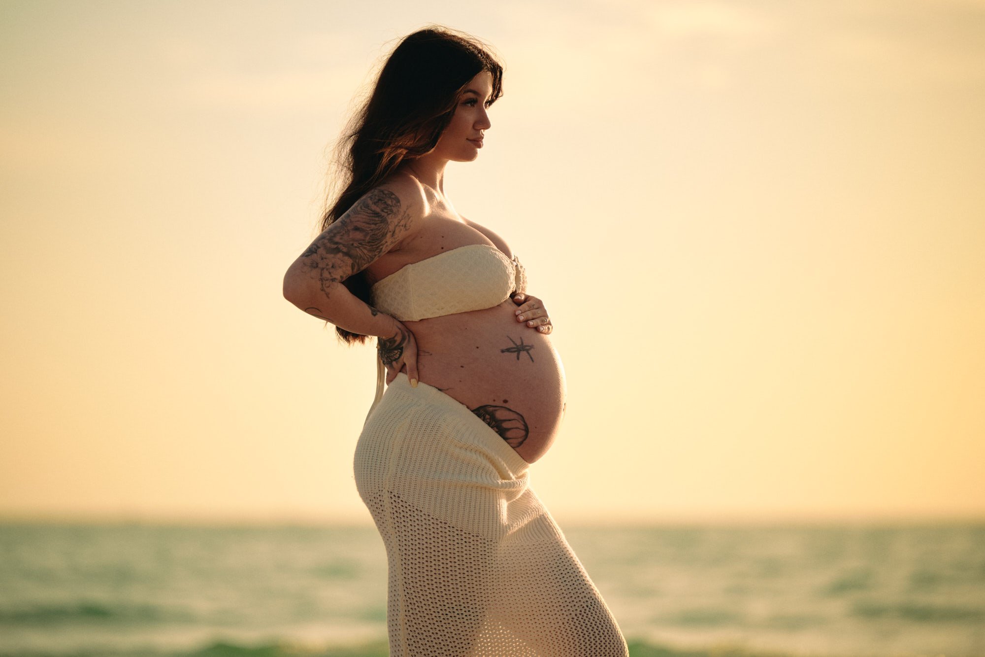 Backlit on the sand in white, tattoos and bump outlined by a hazy Florida sunset.