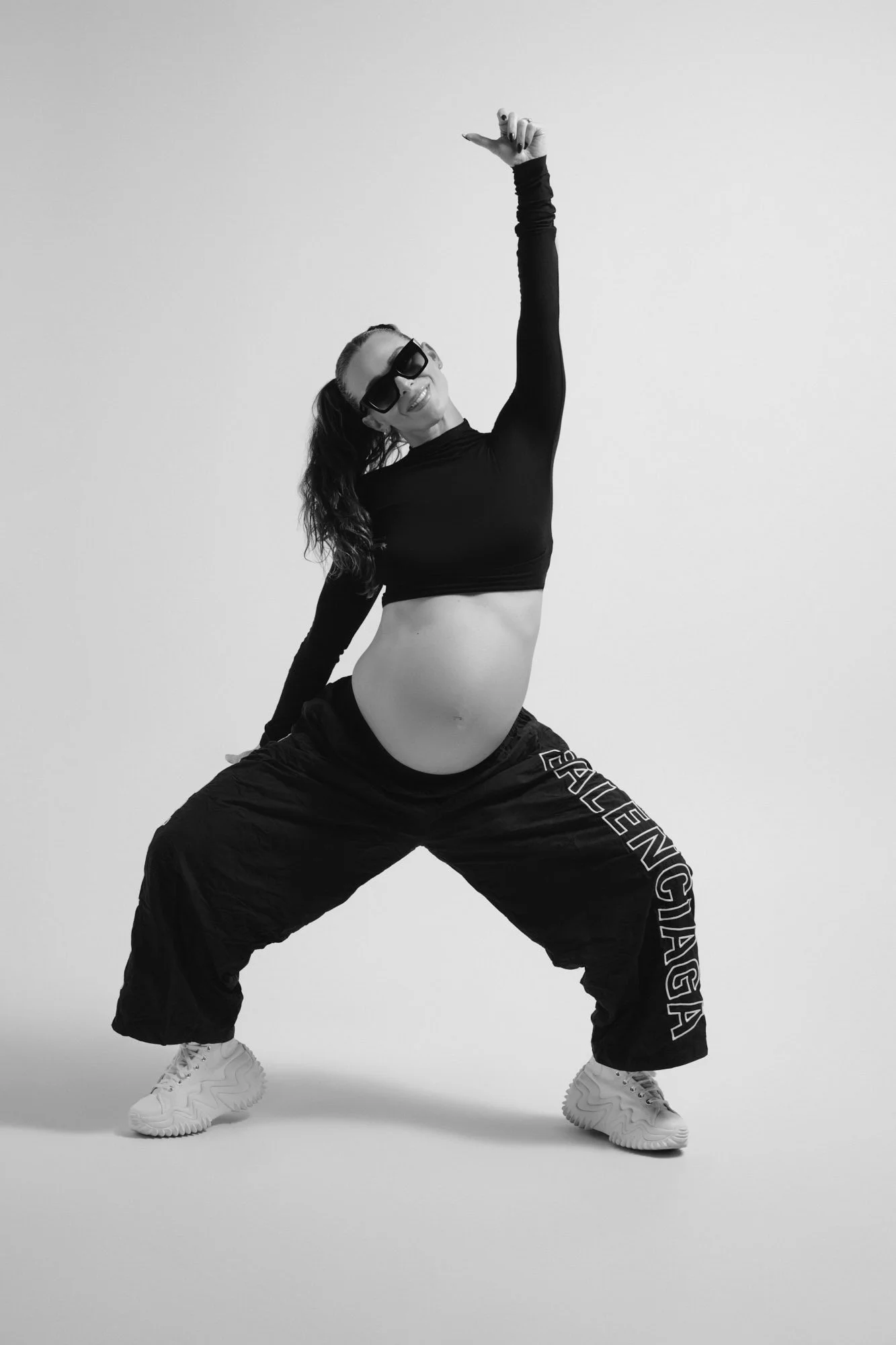 Black and white power pose in track pants and a cropped top, arm reaching high.