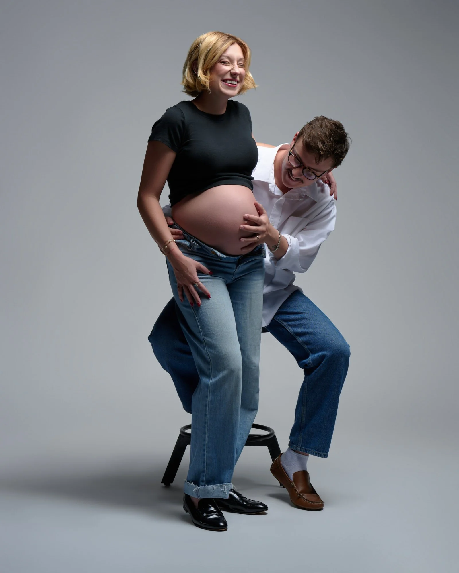 Laughing as her seated partner reaches around to hold the bump.