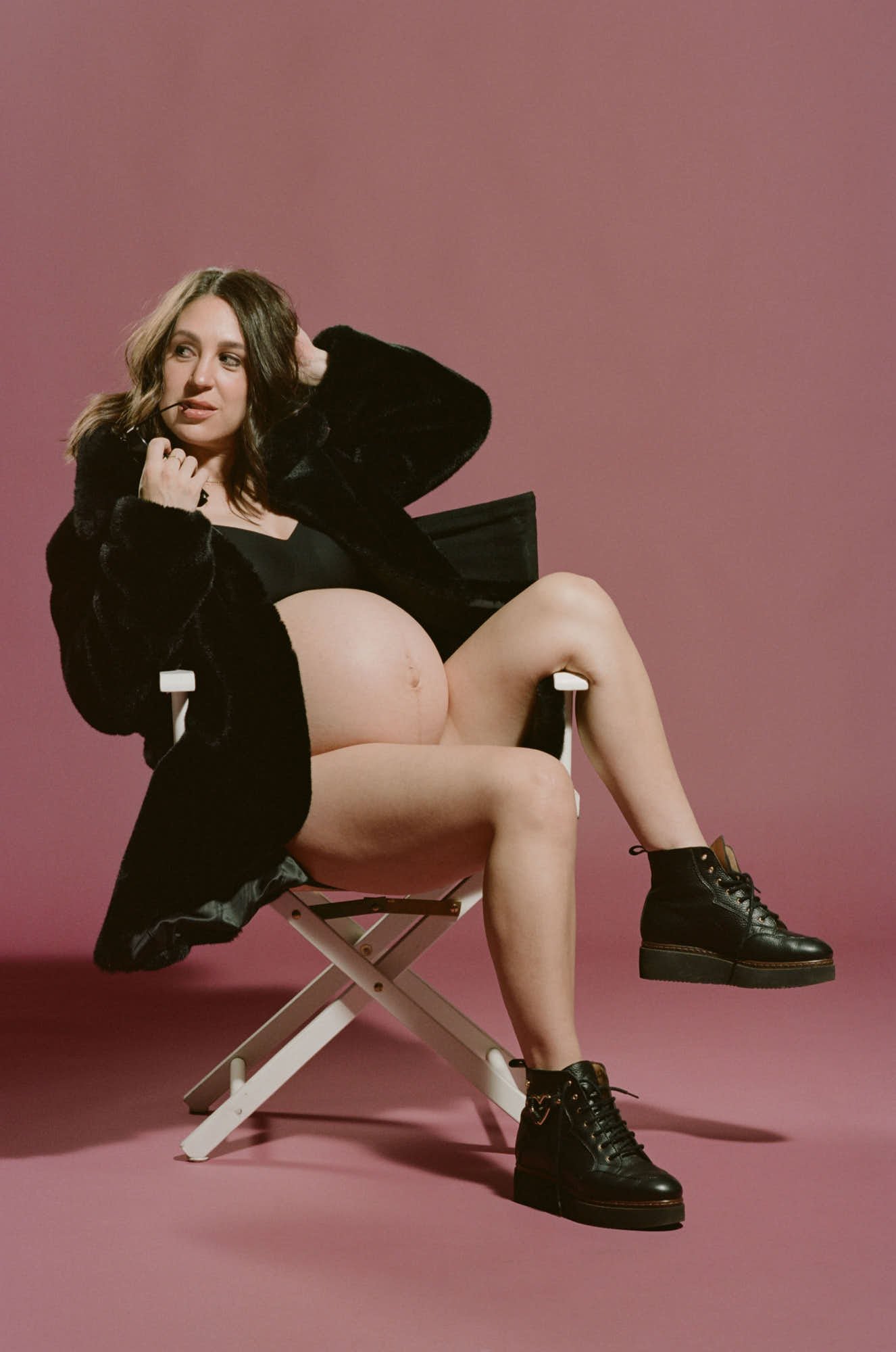 Black blazer and lace-up boots on a director's chair, dusty rose backdrop lit soft behind her.