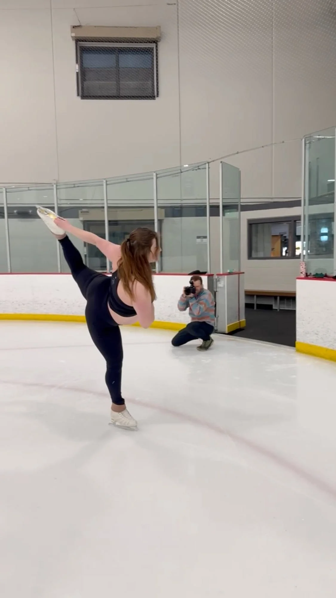 Ethan Herrold crouched at the boards photographing a figure skater on the rink.