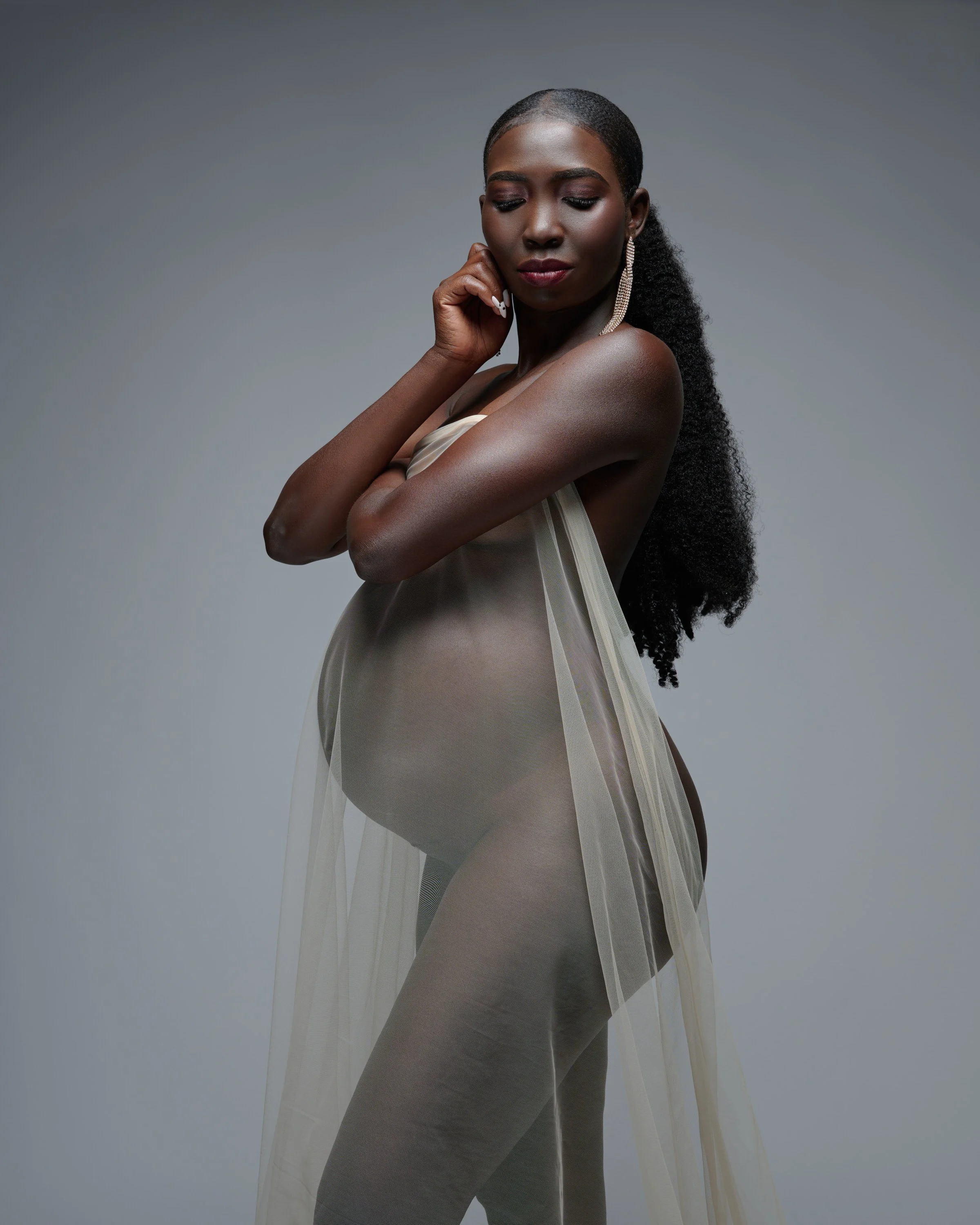 Sheer champagne drape and a long braid, hand raised to her cheek in soft light.