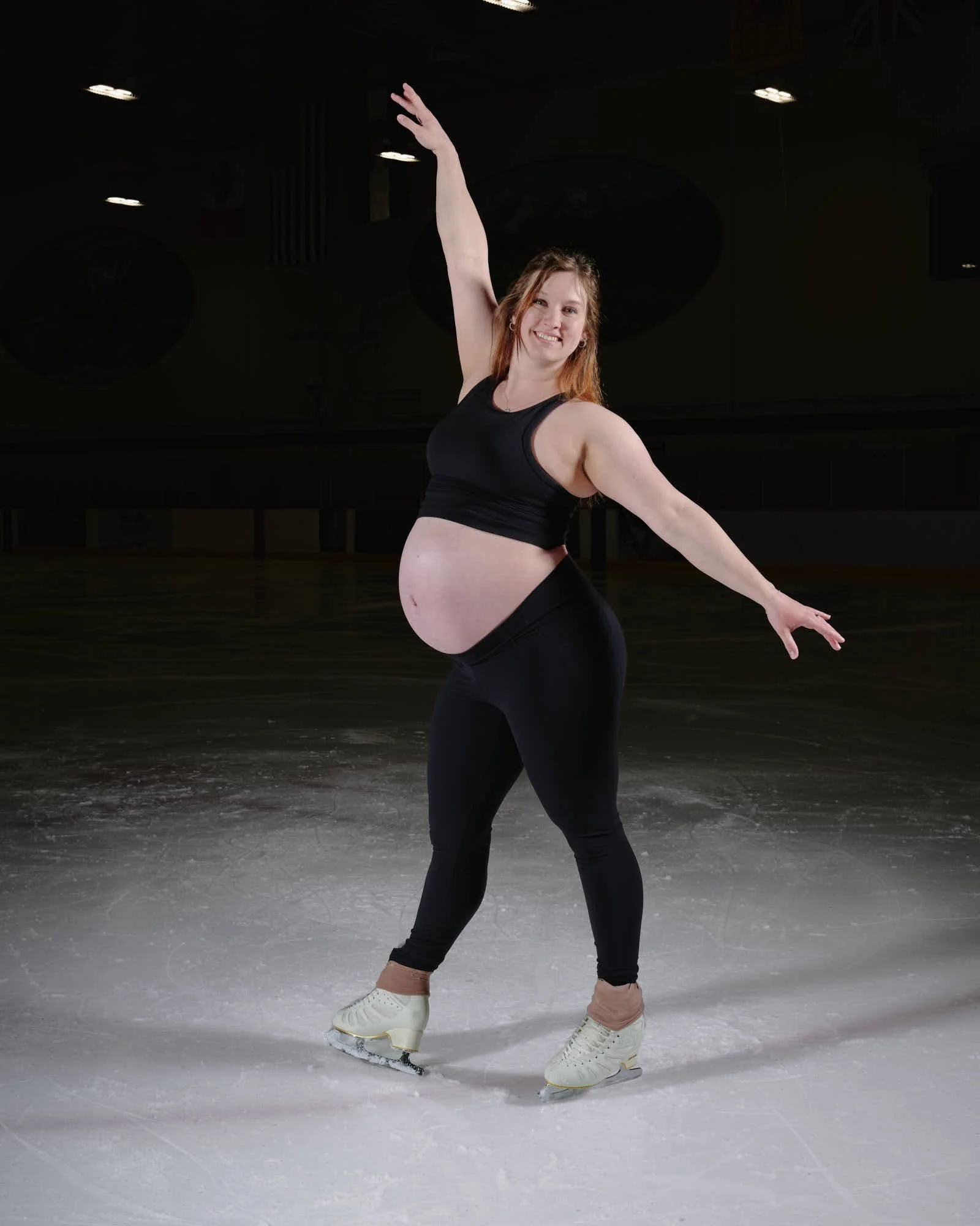 Turning with both arms raised, blades crossed, cold rink light on the bump.