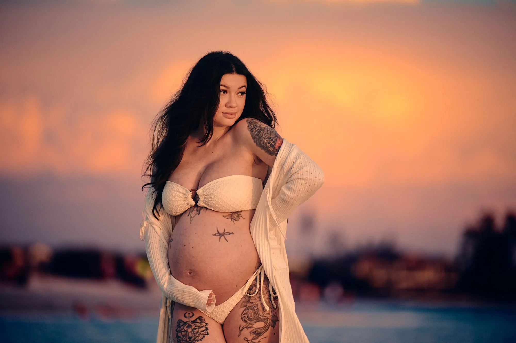 Cream cardigan and a tattooed bump at sunset, sky burning orange over the Gulf.