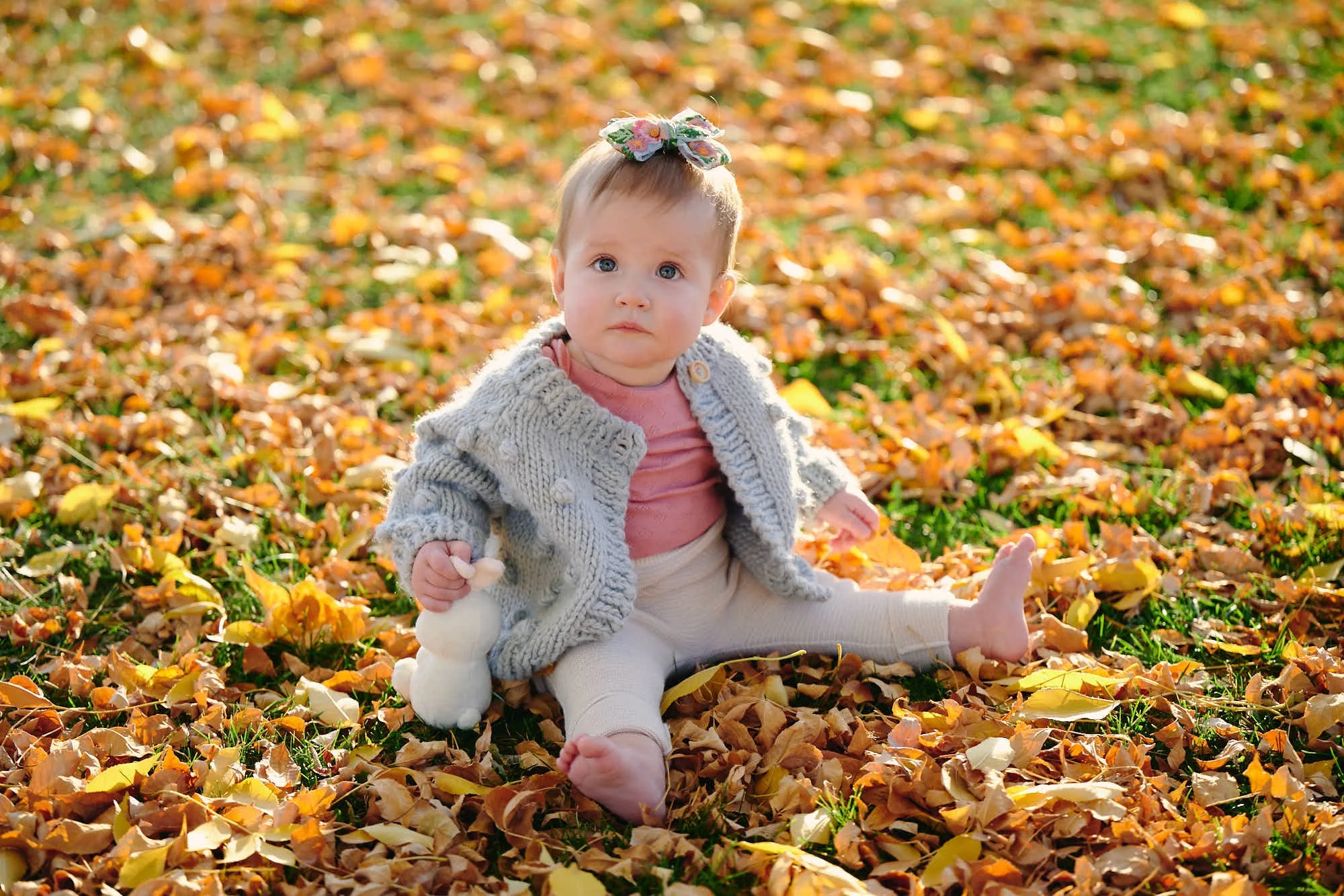 Baby in a grey knit cardigan sitting among fallen golden leaves during a Colorado fall family session.