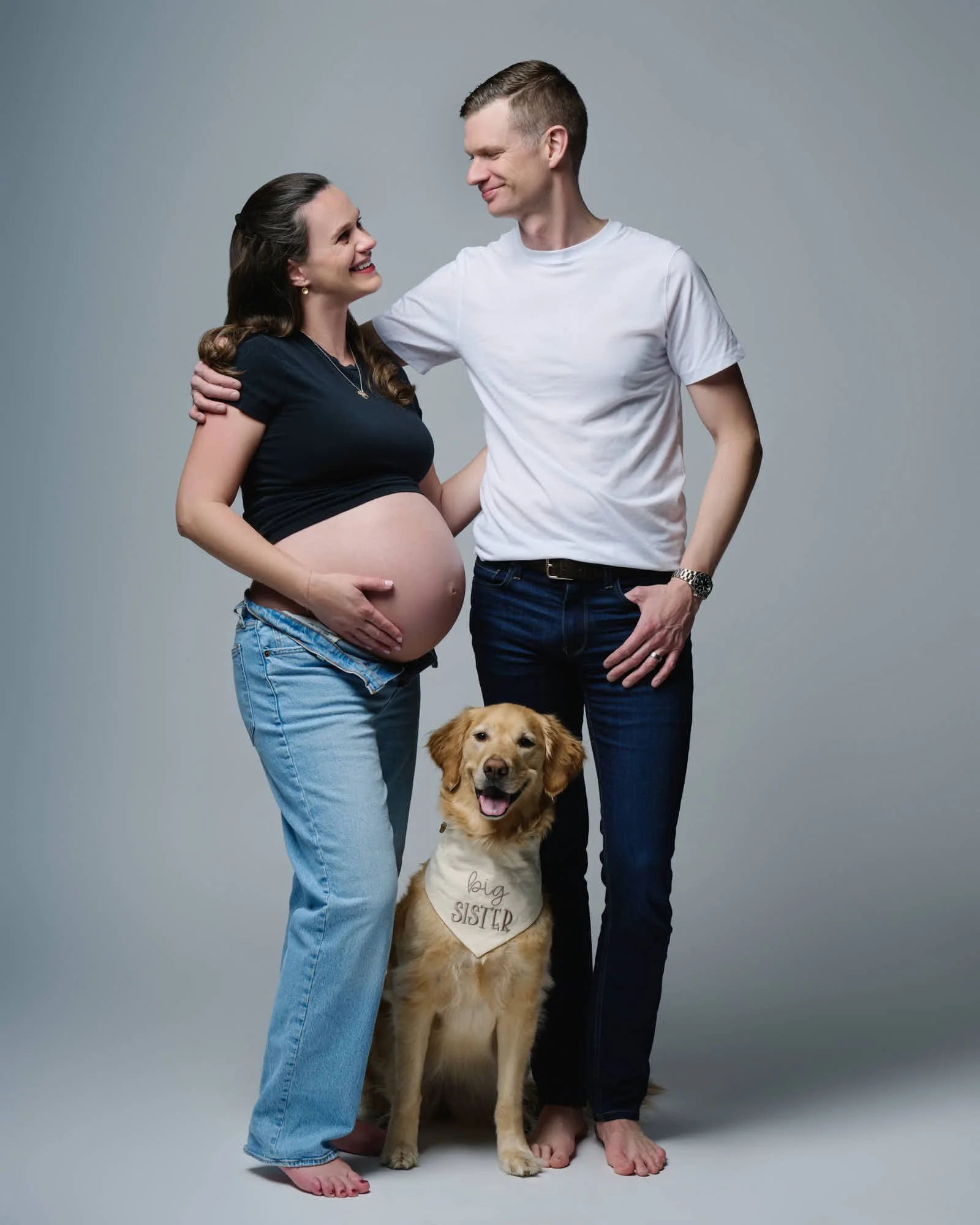 Expecting couple in the studio with their golden retriever.