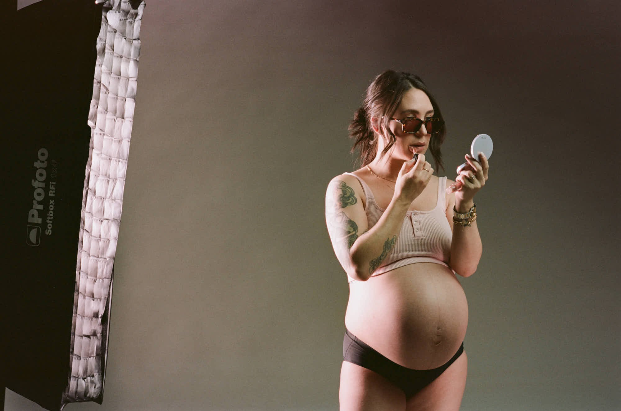 Lipstick and a hand mirror between setups, softbox glowing at the edge of the frame.