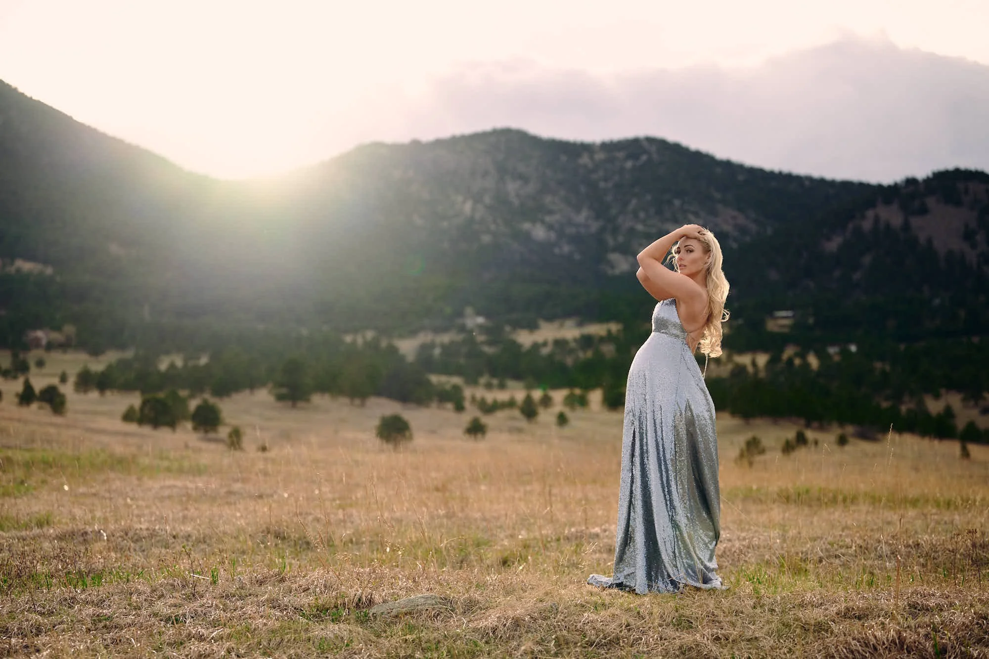 Flowing silver gown and a hand lifted to her hair at golden hour below the Colorado foothills.