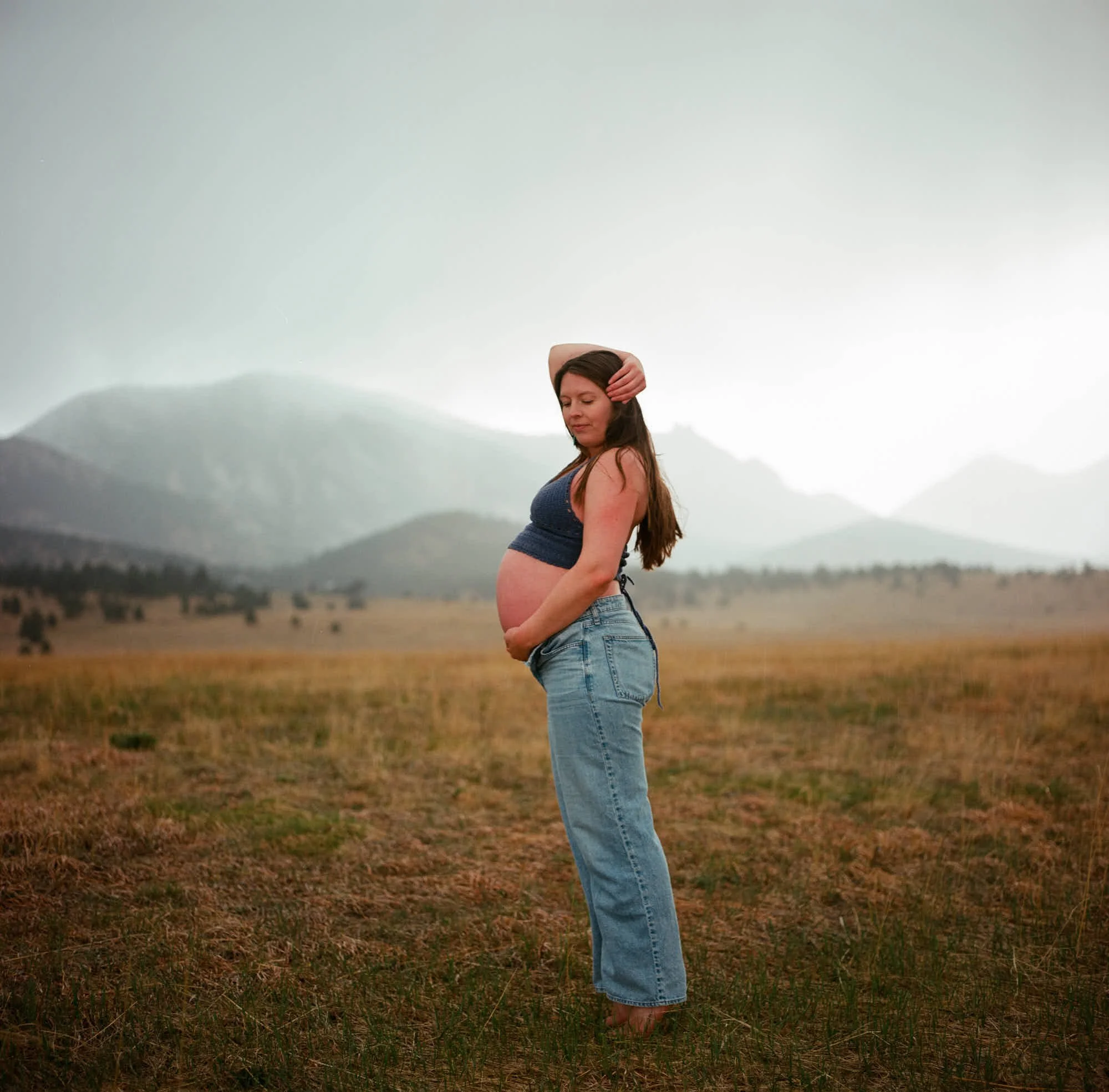 Grainy fine art film frame, profile in a charcoal tank against misty peaks.