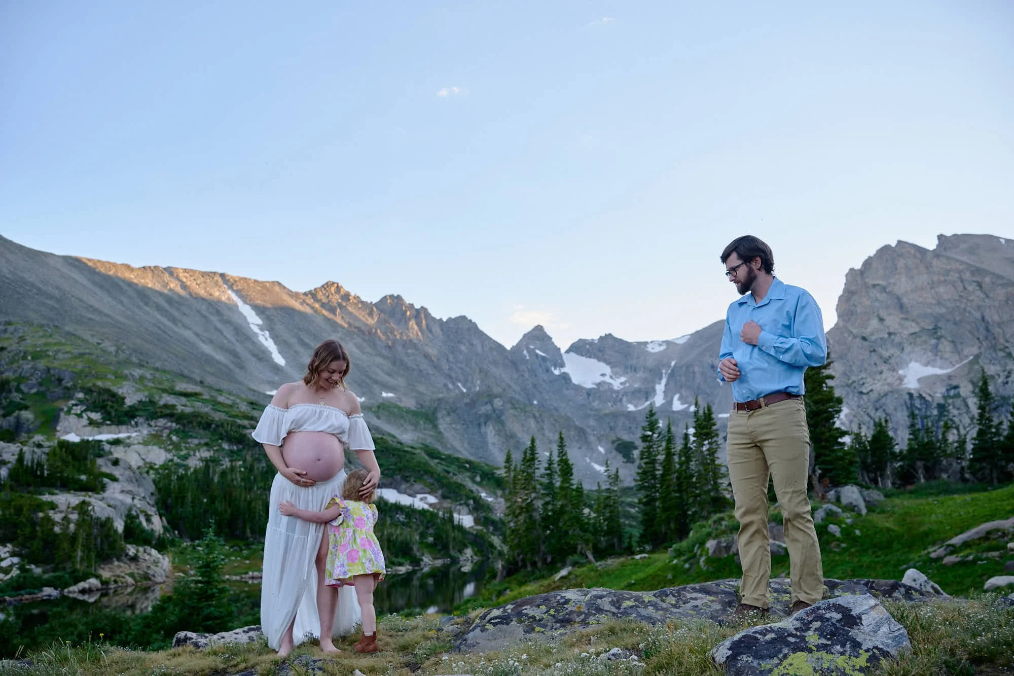 Expecting mother, her husband and their toddler on an alpine ridge at sunset.