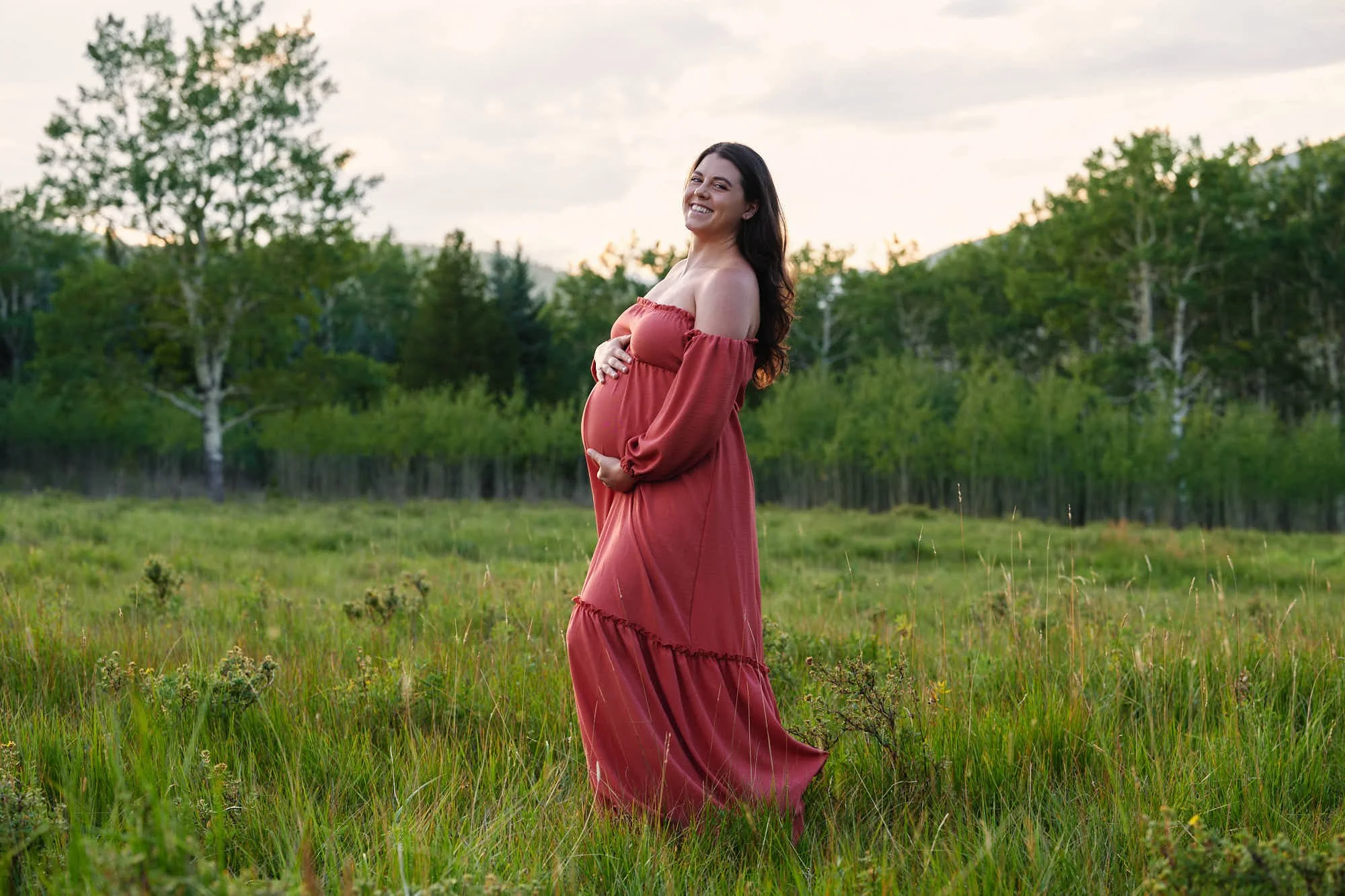 Rust off-shoulder tiered maxi dress in a tall green meadow framed by aspen trees.