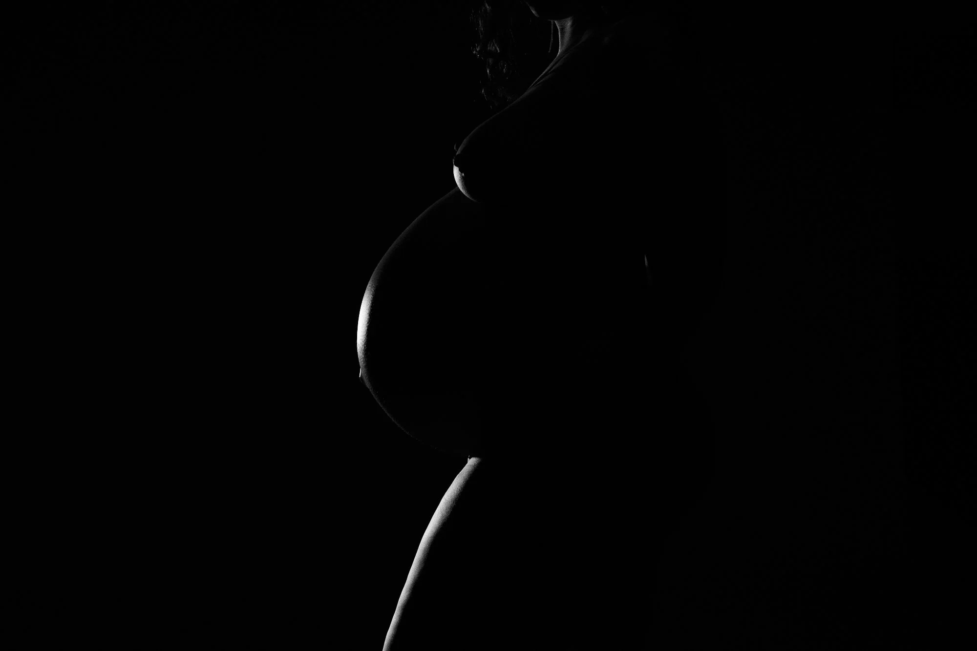 Black and white close-up of a bare baby bump in profile, sculpted with studio light.