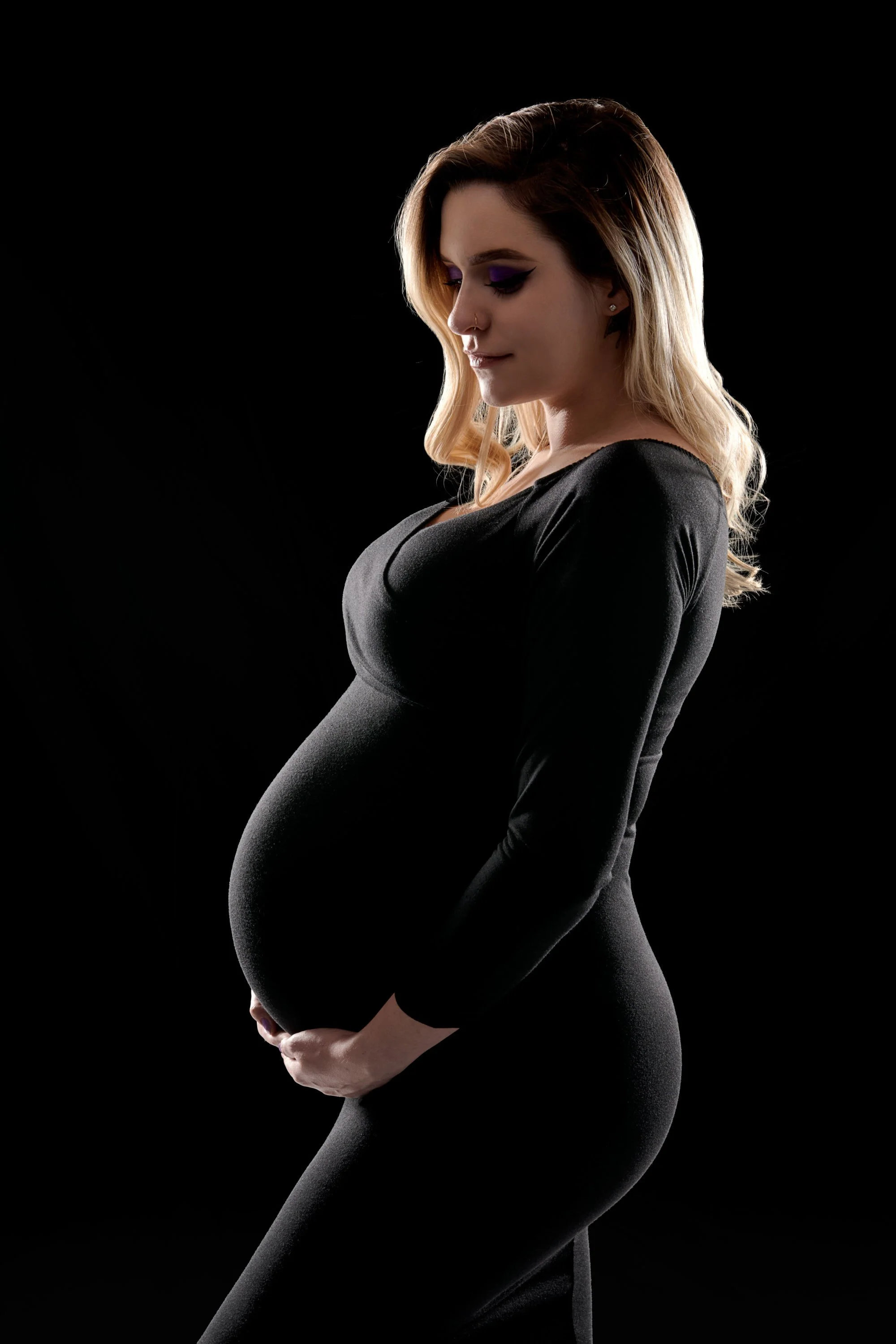 Fitted black dress with warm rim light tracing the profile and bump.
