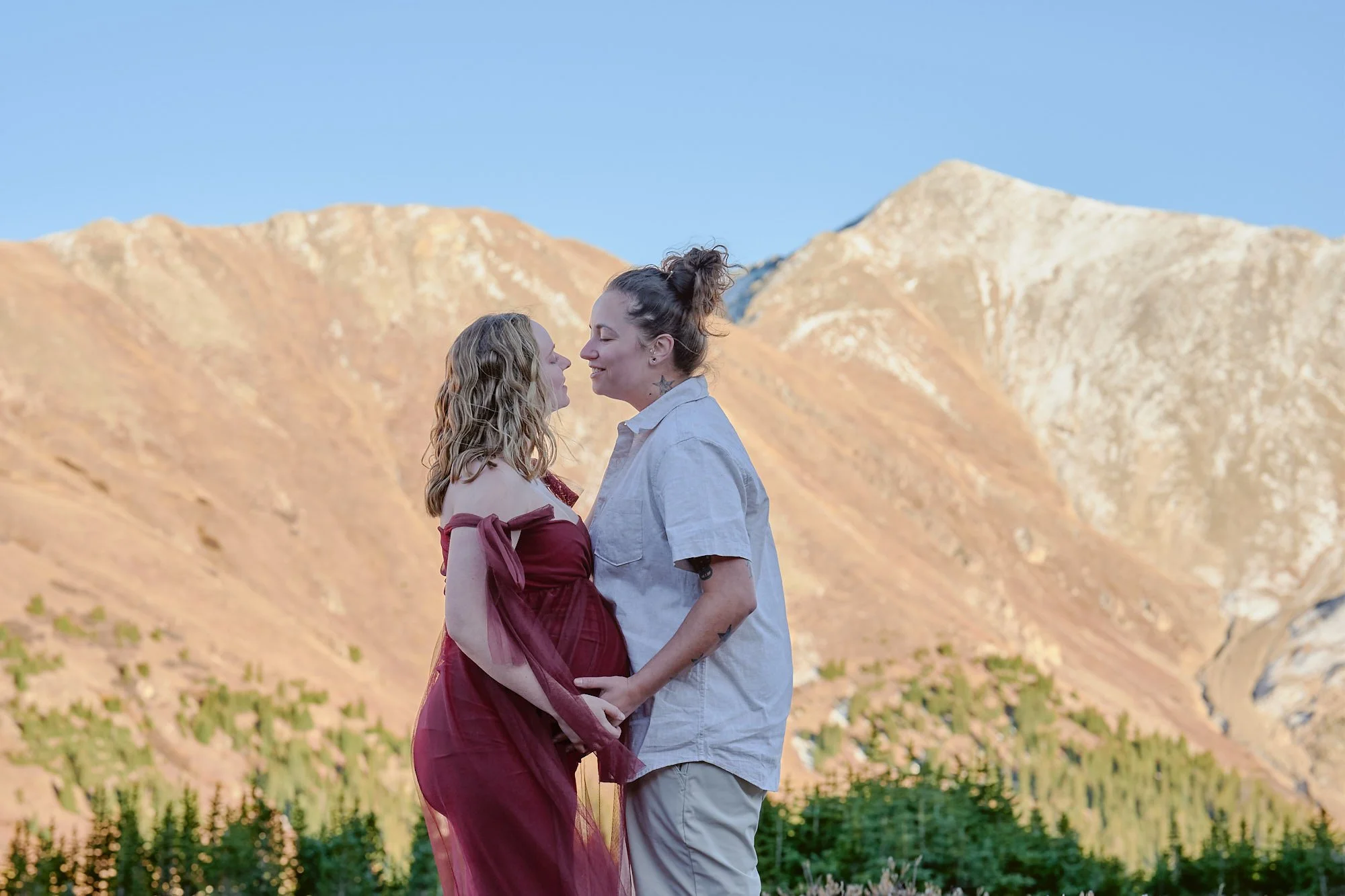 Expecting same-sex couple among golden banded rock formations, heads together.
