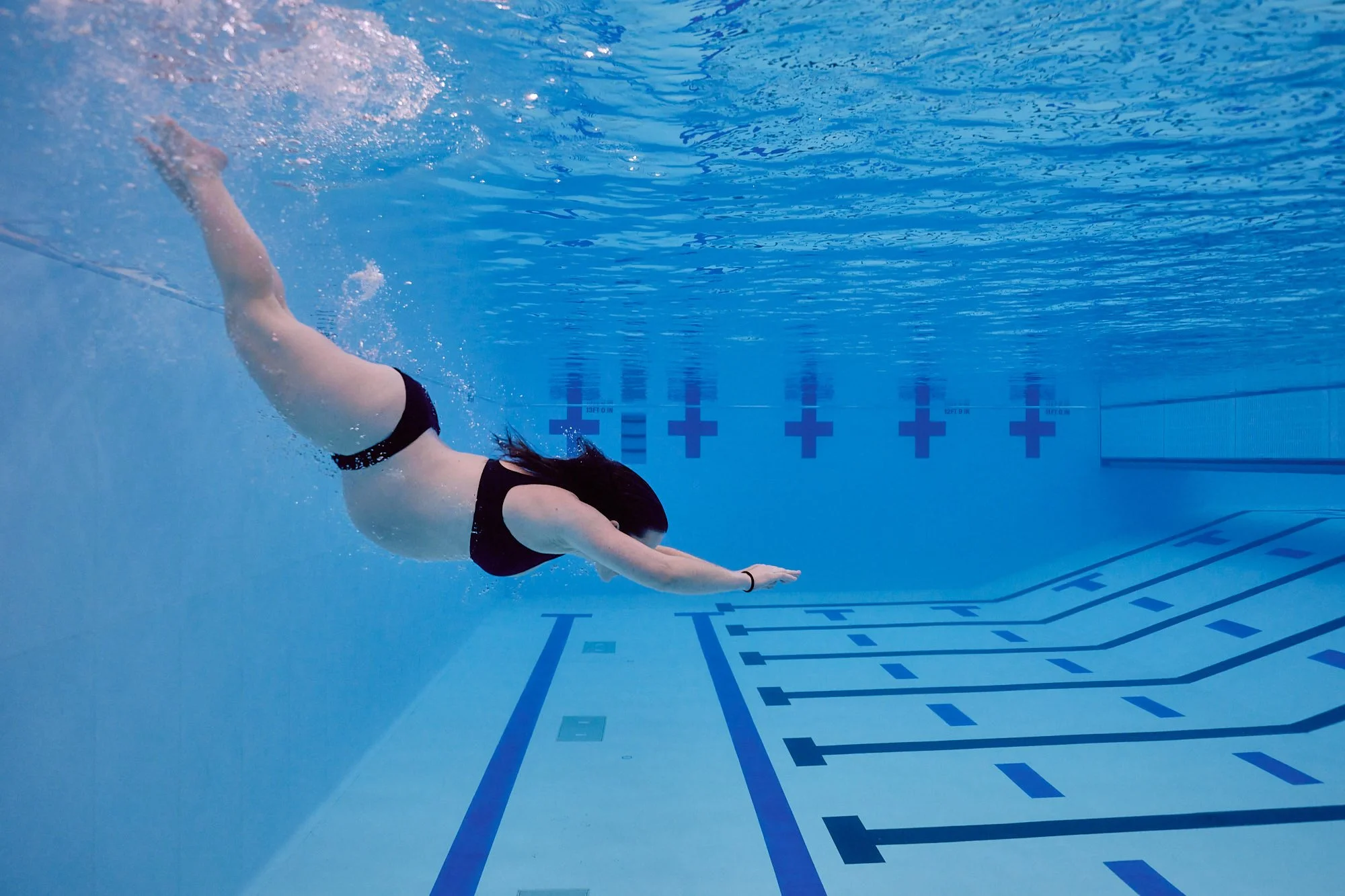 Underwater frame of a pregnant diver streamlined through blue water after entry.