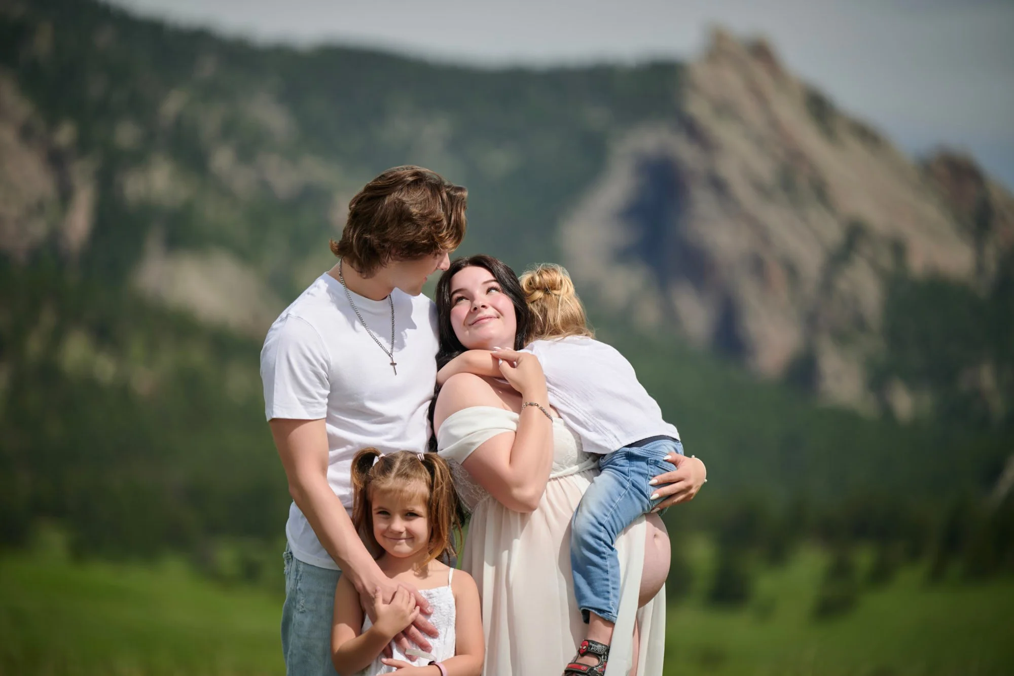 Family of four curled together on a green hillside beneath rocky peaks.