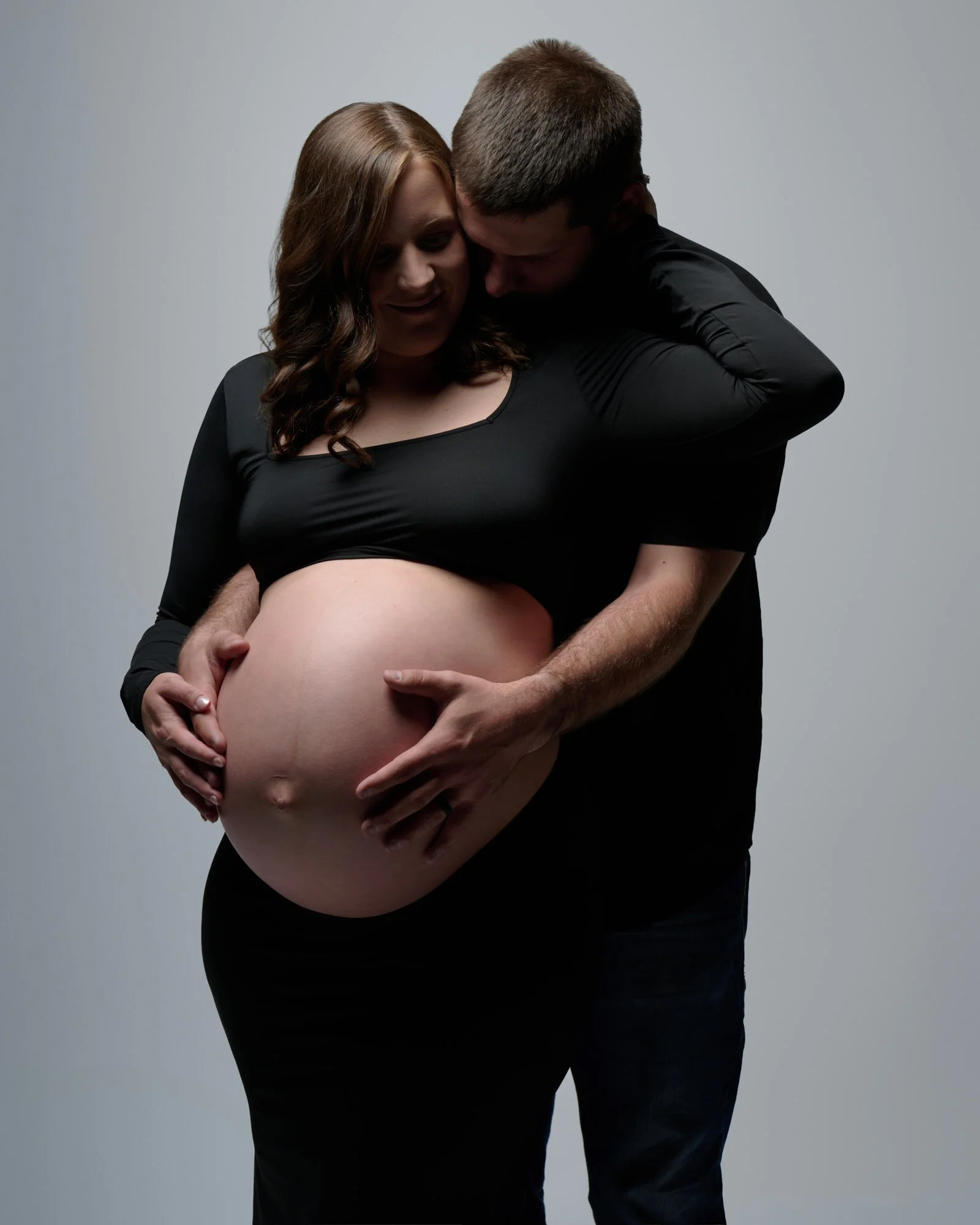 Partner wrapped close behind a mother in black, bare bump front and center.