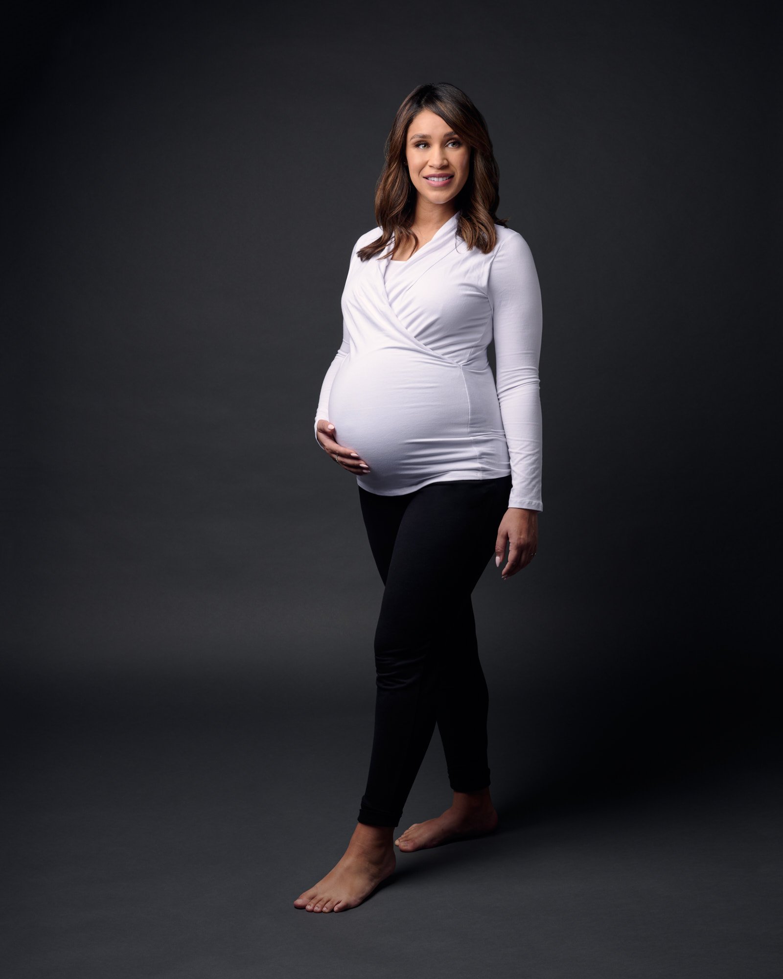 Side profile maternity portrait in white top and black skirt on charcoal studio backdrop