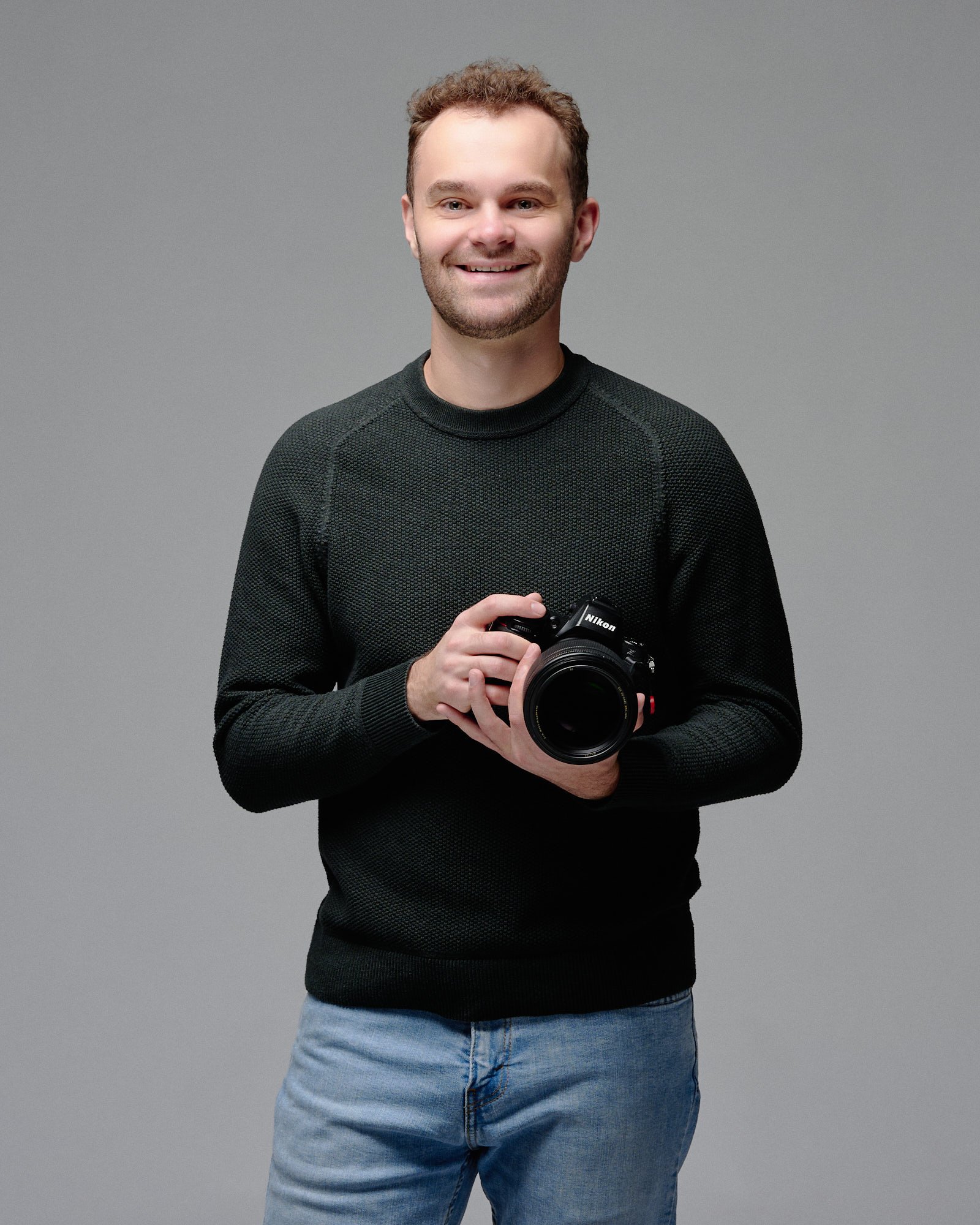 Ethan Herrold, Denver maternity photographer, smiling with his camera in his Denver photo studio.