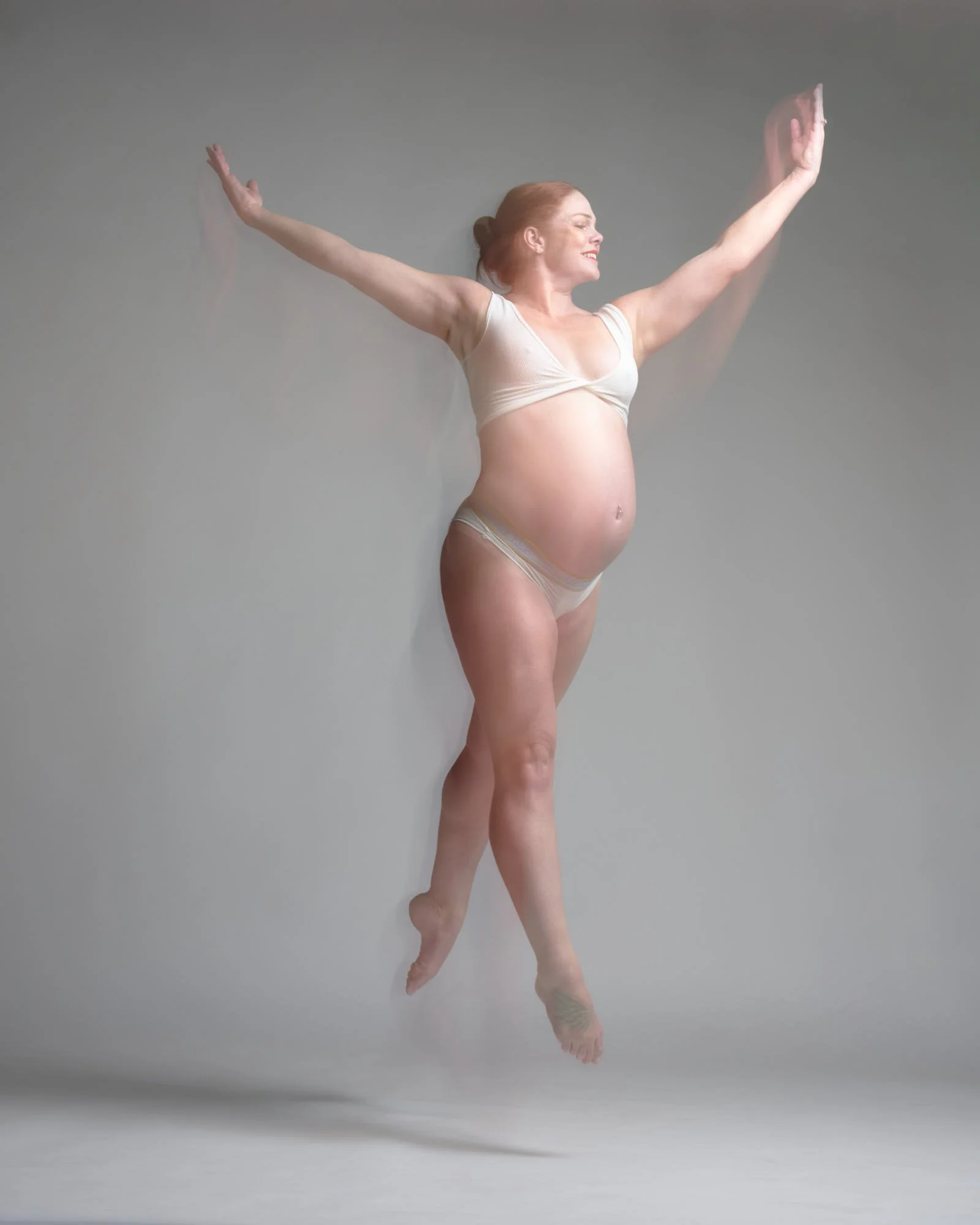 Expecting mother leaps mid-air with motion-blur trails, celebrating her pregnancy in the Denver maternity photo studio.