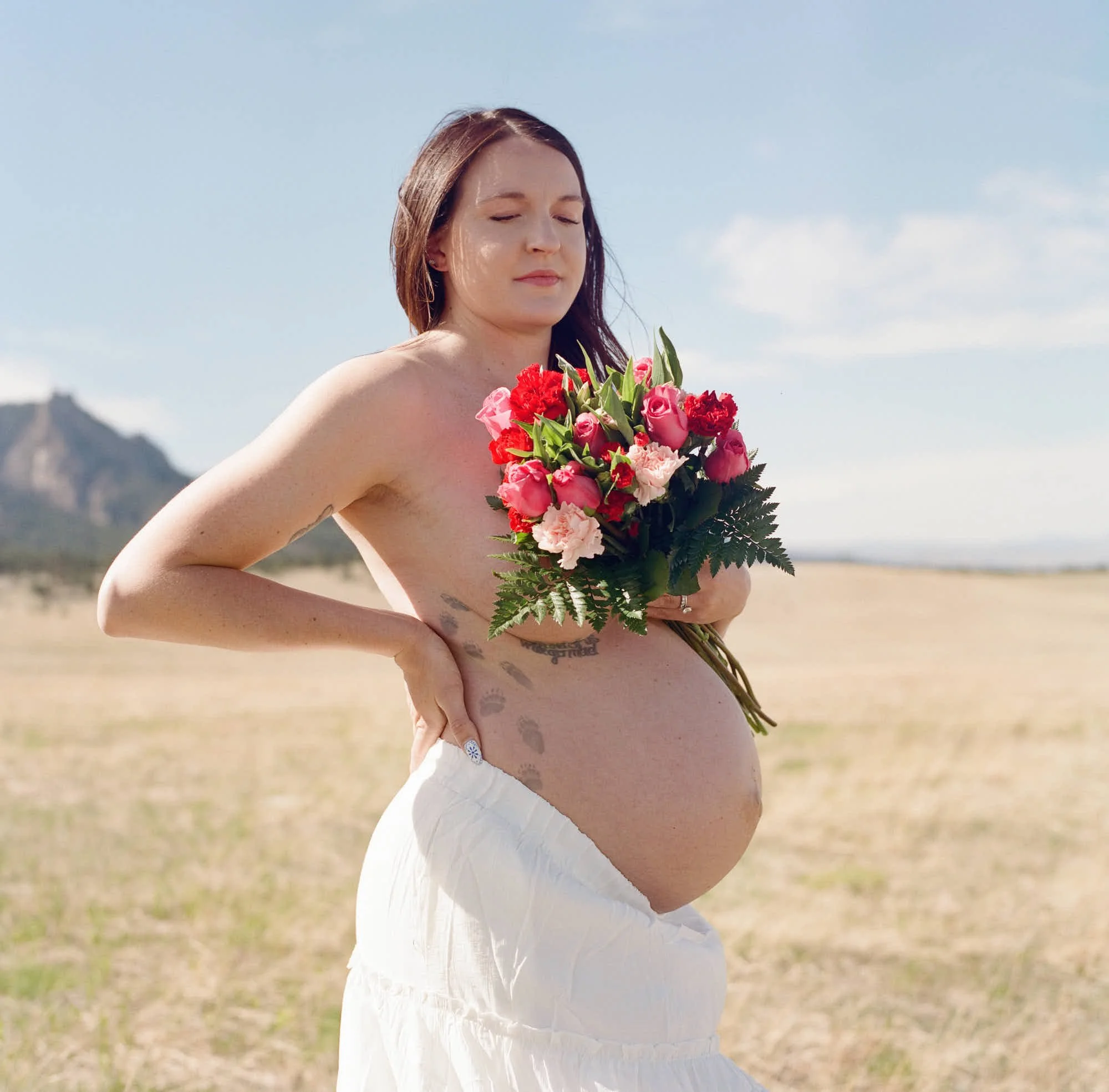 Bouquet held against a bare bump, white skirt and dry gold grass under the foothills.