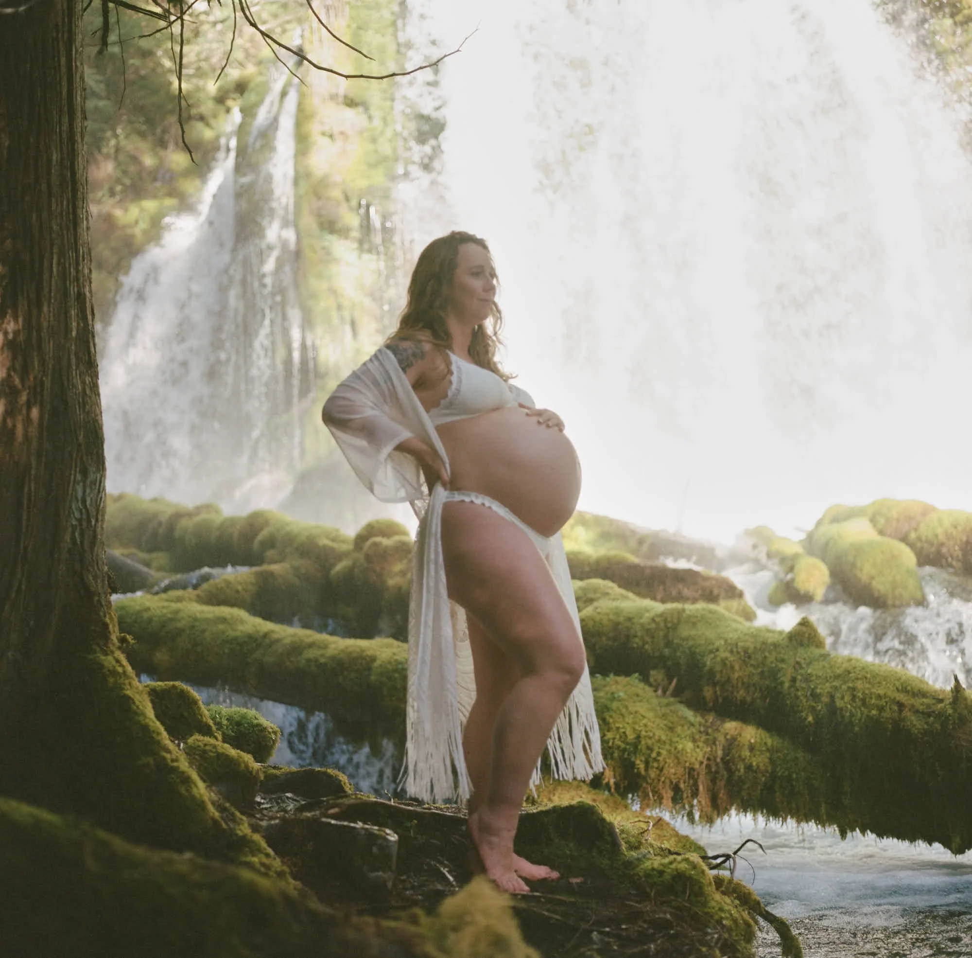 White fringed robe open over the bump beneath a Cascades waterfall, moss glowing green.