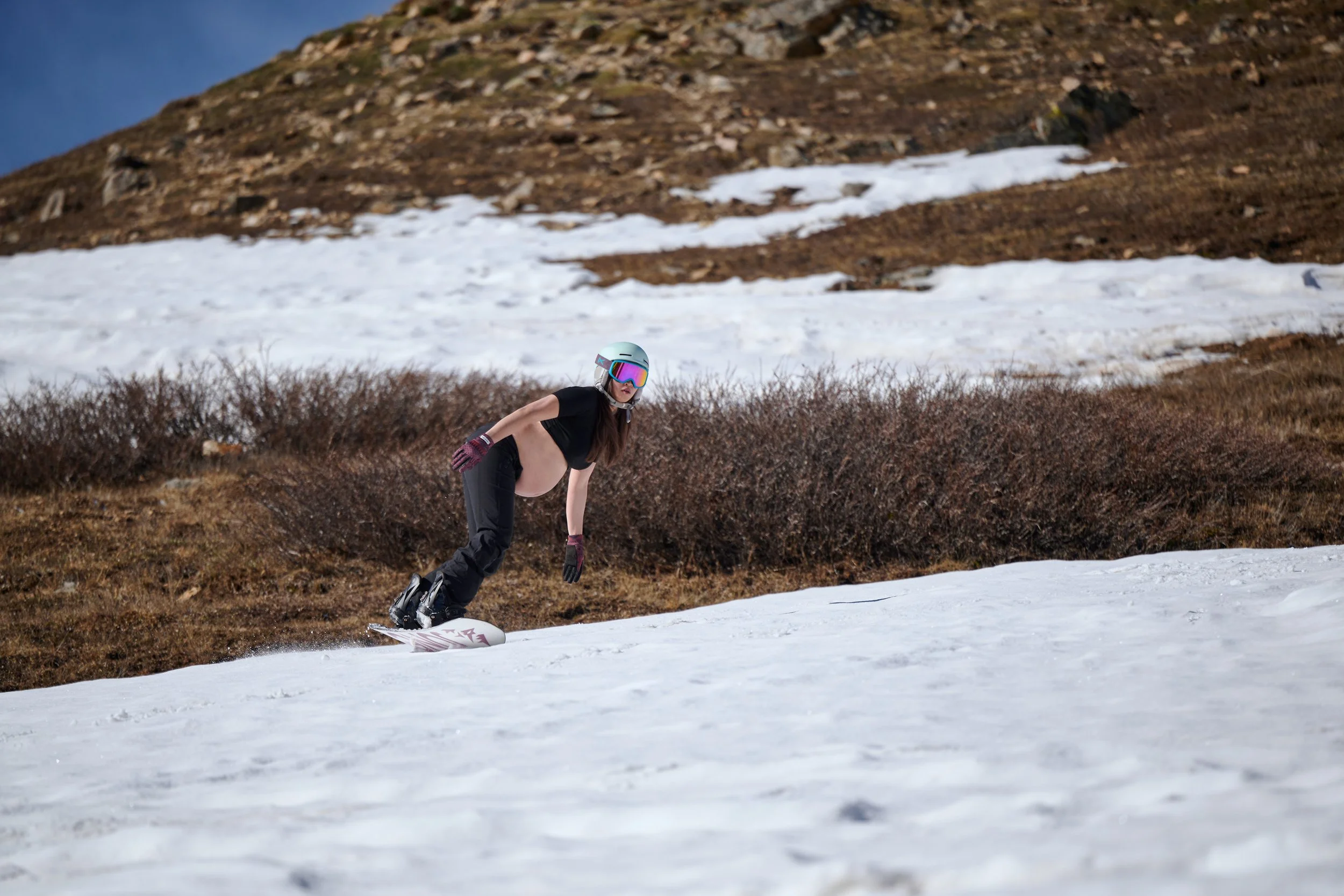 Skier tucked low across the slope where snow gives way to bare Colorado tundra.
