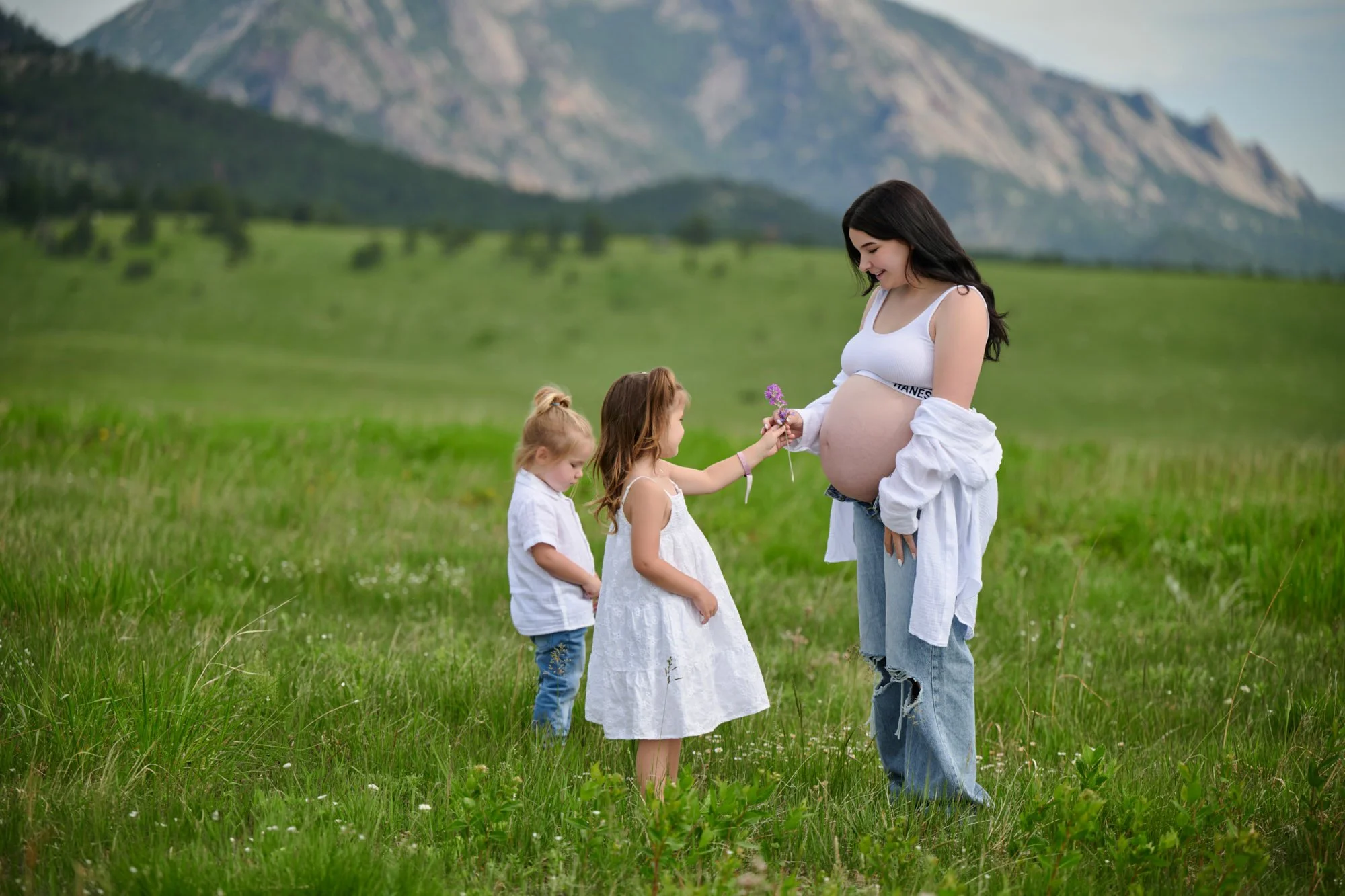 Two little ones in white bring mama wildflowers in a green mountain valley.