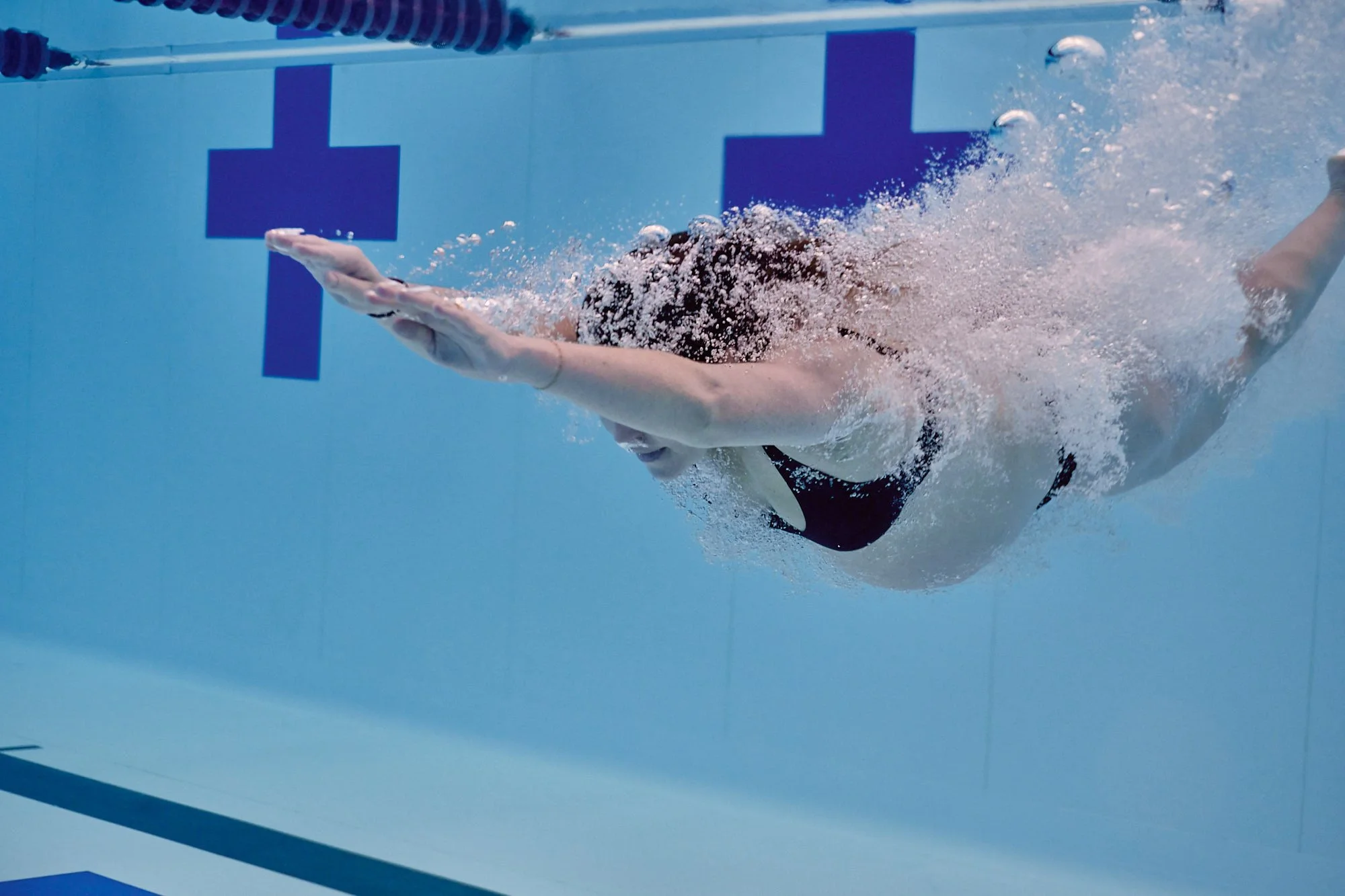 Underwater entry trailing a curtain of bubbles across the blue tiled pool wall.