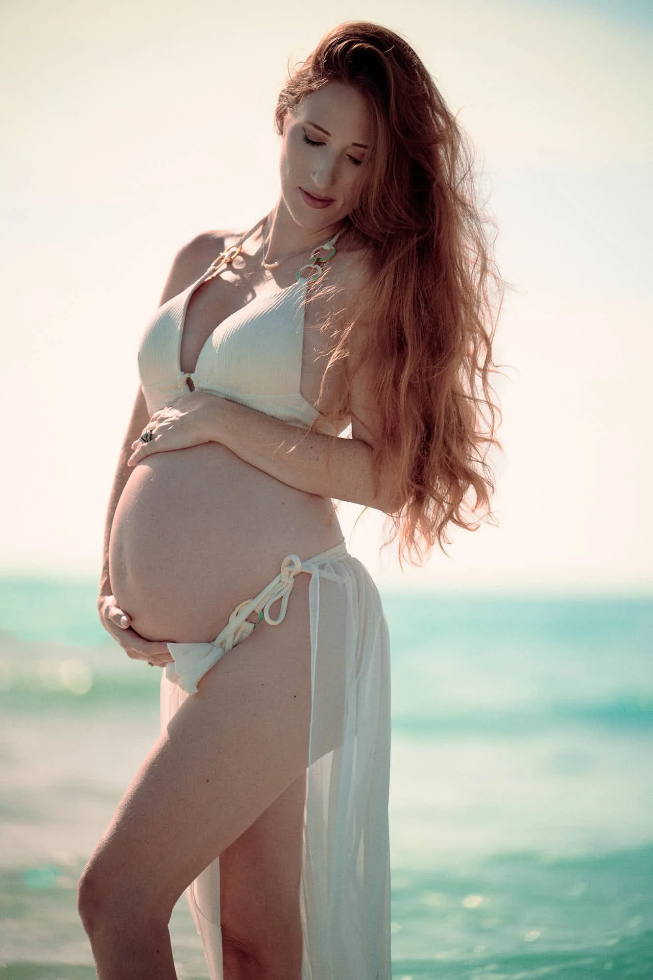 White two-piece and a sheer wrap in the Florida surf, sun flaring off the water.
