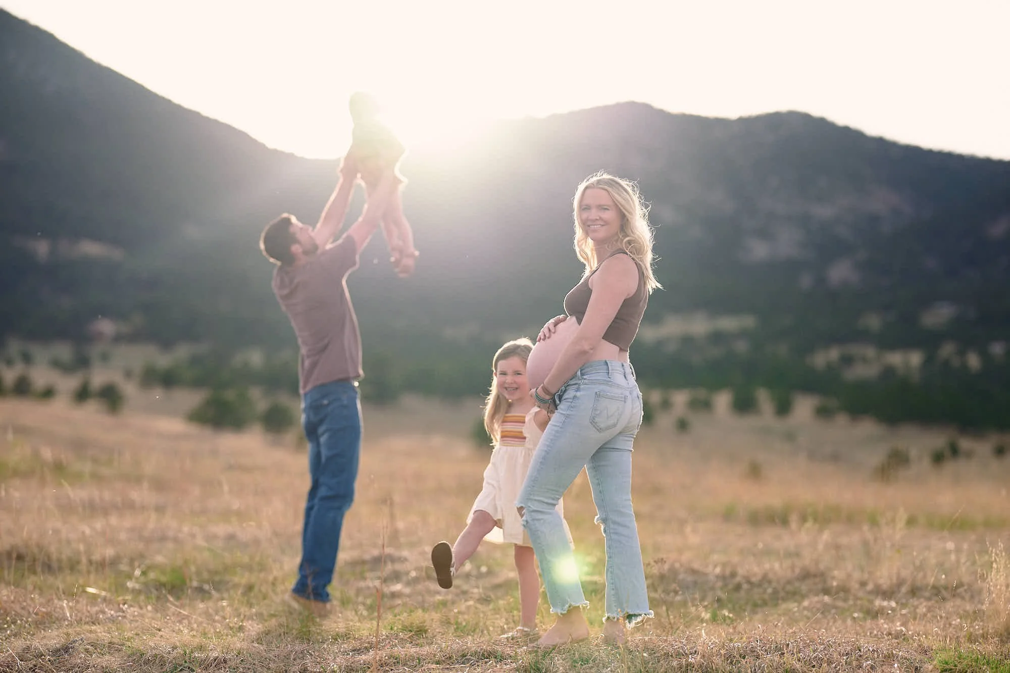 Dad tosses the little one skyward while mom and big sister laugh in the sunset field.