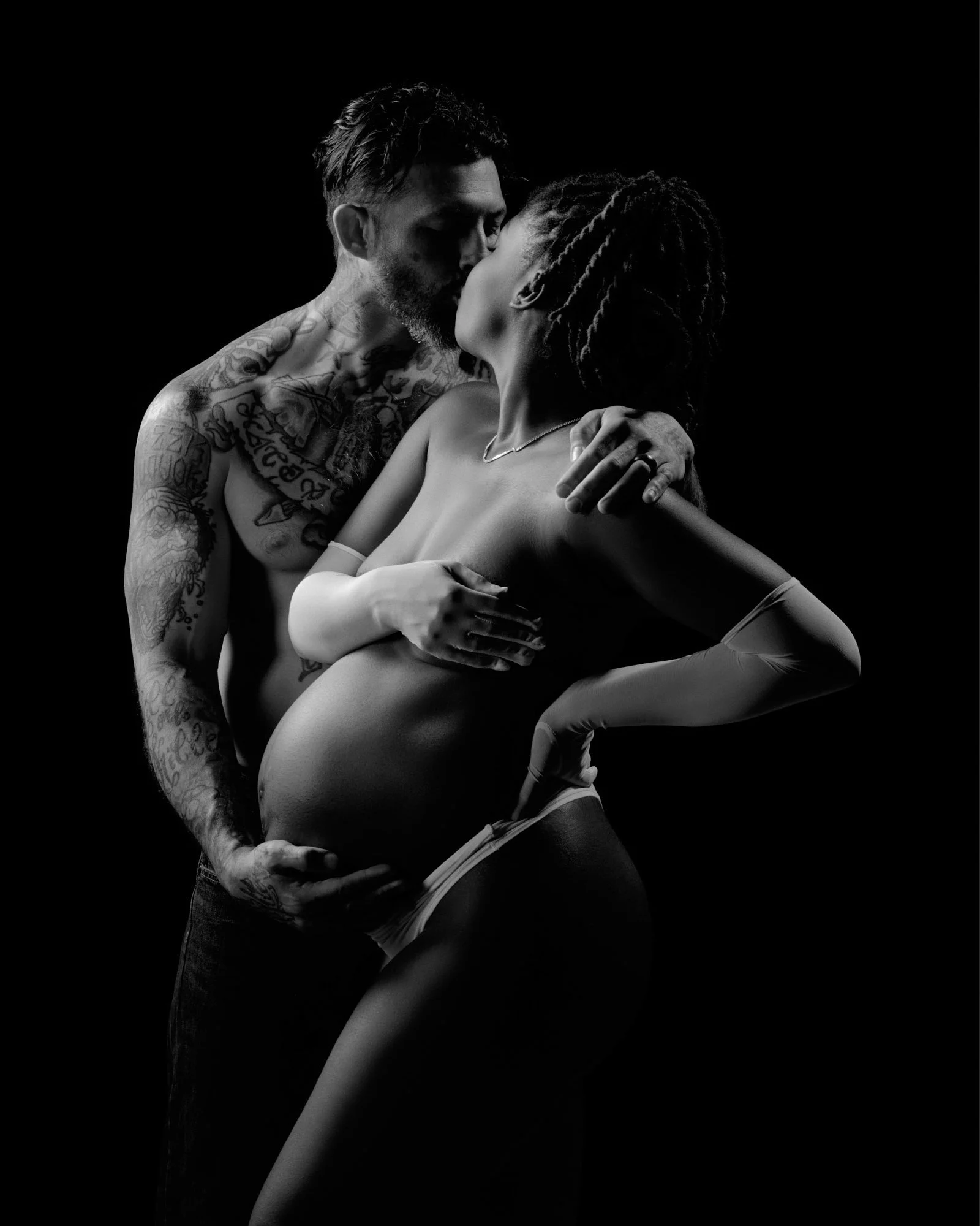 A kiss to her temple in black and white, tattoos and quiet intimacy.