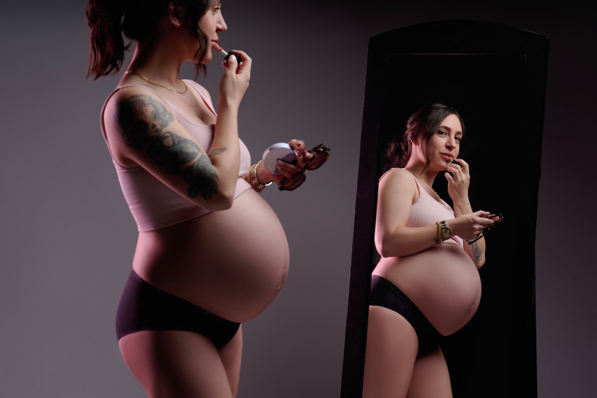 Applying lip gloss at a full-length mirror, her reflection facing the camera.