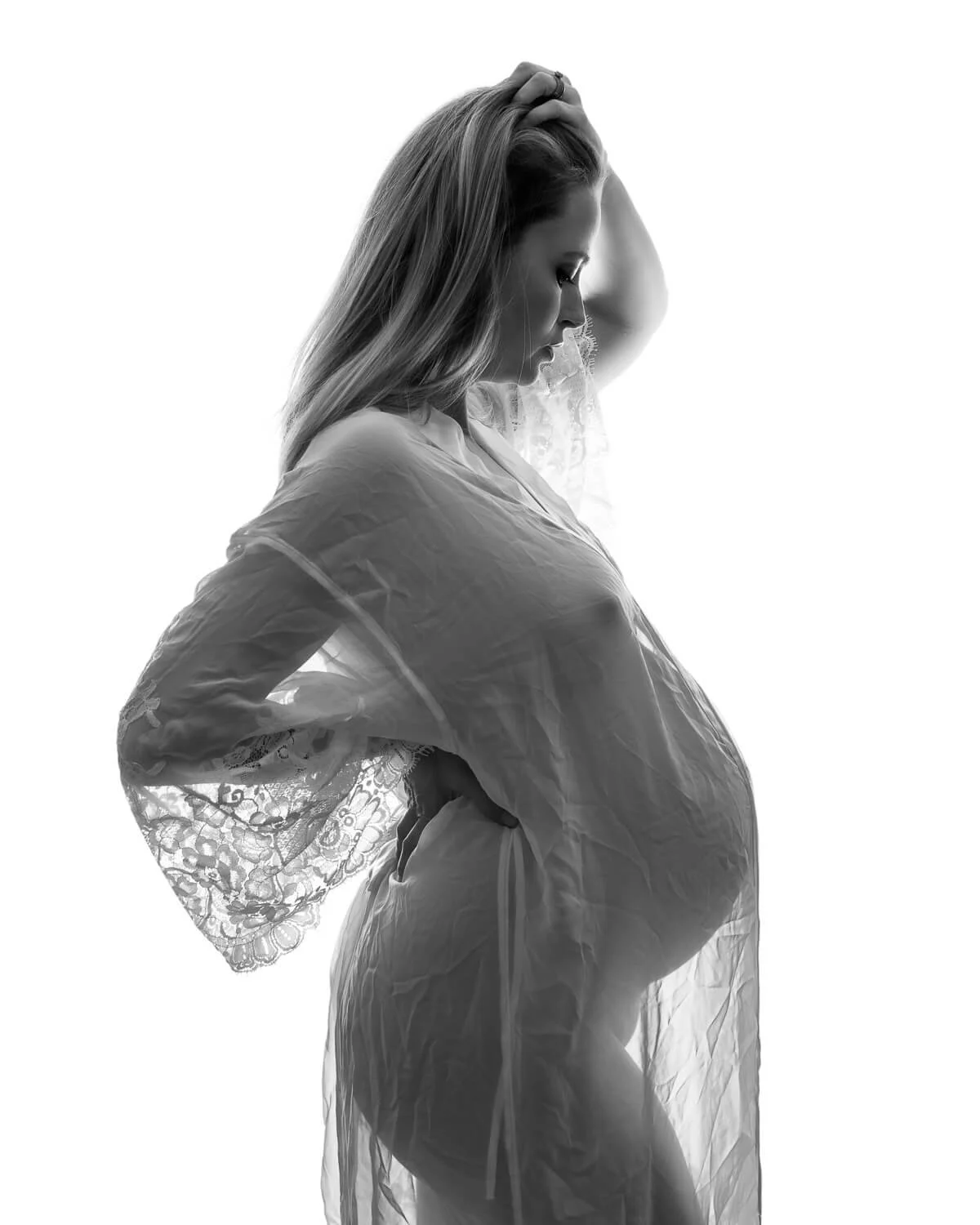 Black and white frame in a sheer lace robe, soft light tracing the bump.